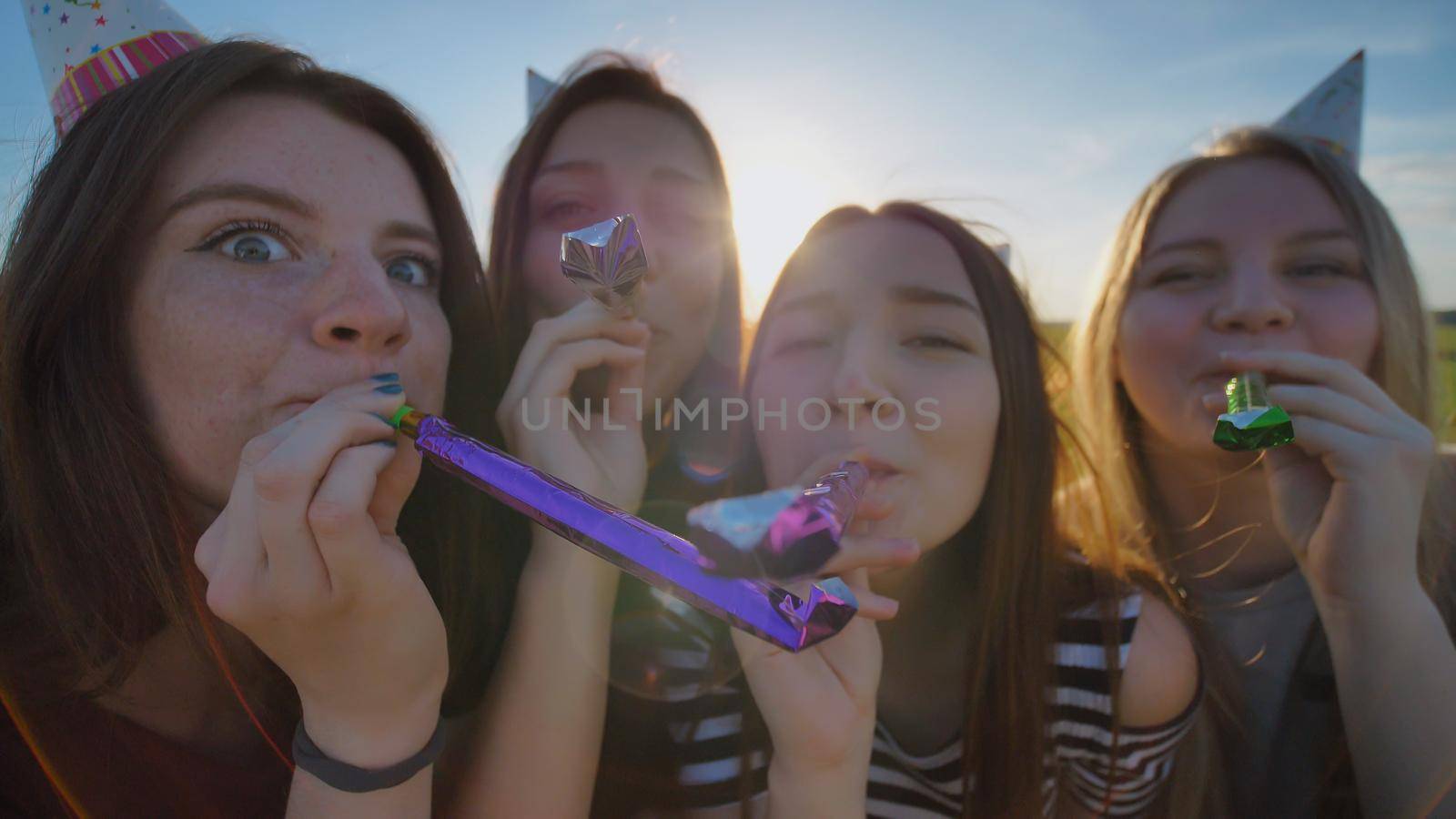 Girls cheer and celebrate the holiday outdoors and blow out toys with caps on their heads