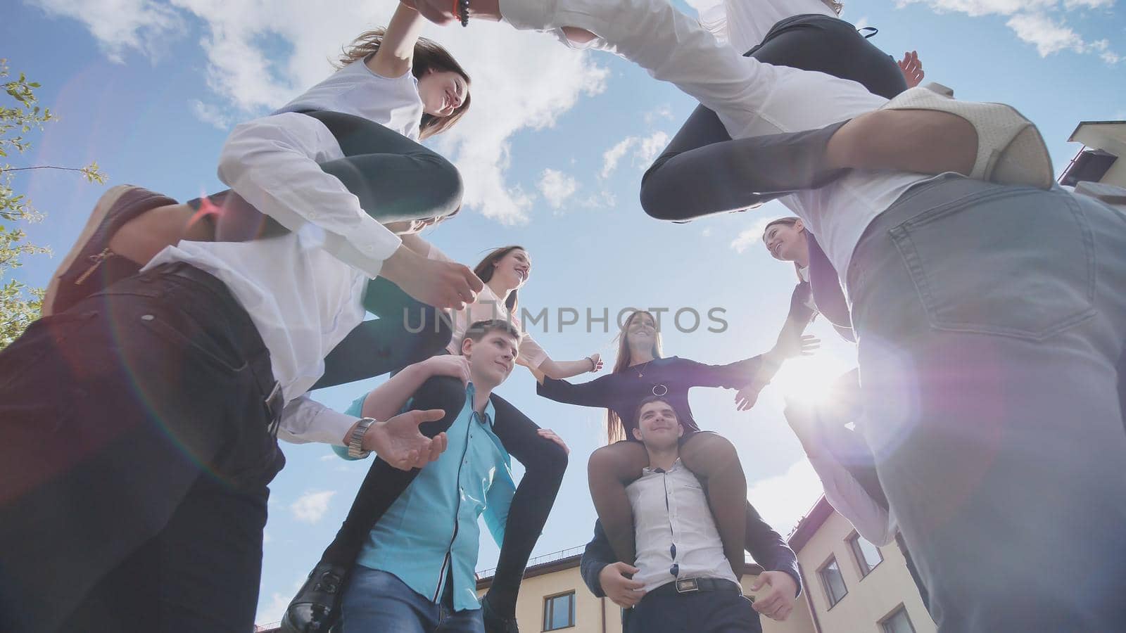 The girls sit on the shoulders of the guys and hug together. Happy friends are senior pupils