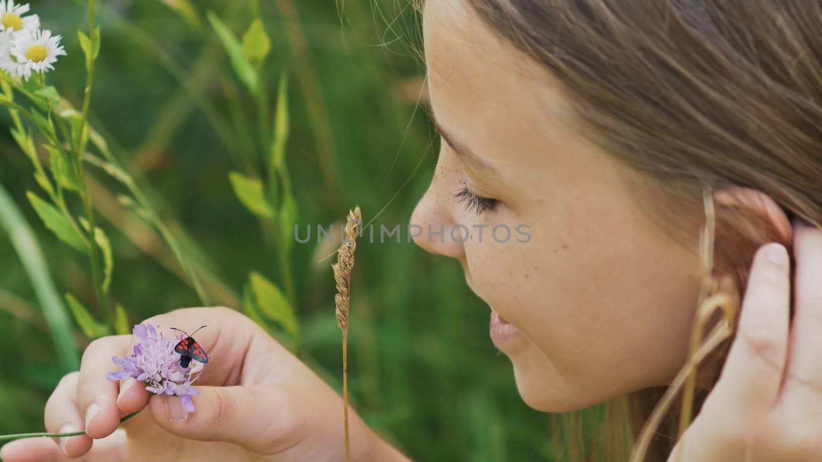 Teenage girl admires a moth on a flower. Warm summer day