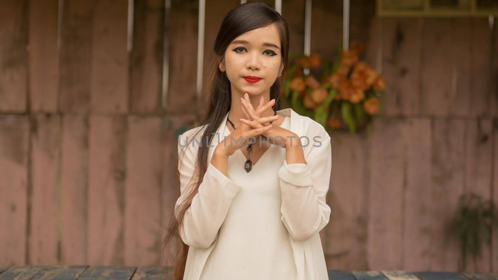 Vietnamese young brunette woman posing against the wall with artificial roses