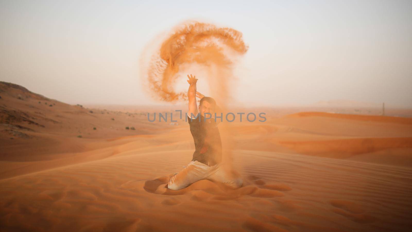 The guy throws sand over himself in the desert. The desert is next to Dubai. UAE