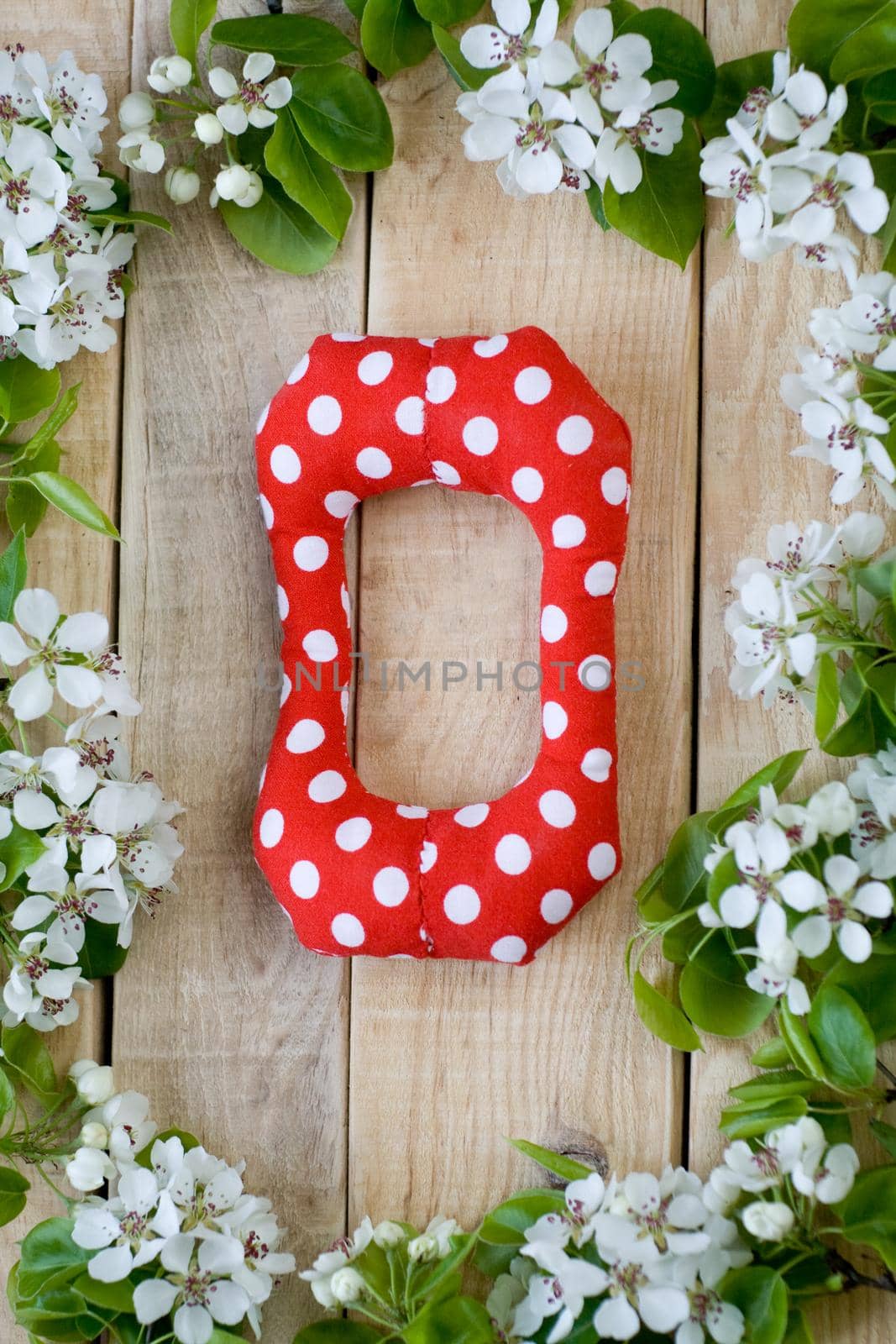 Natural wooden background with white flowers fruit tree. In the middle is the letter О, is made of red polka dot fabric.