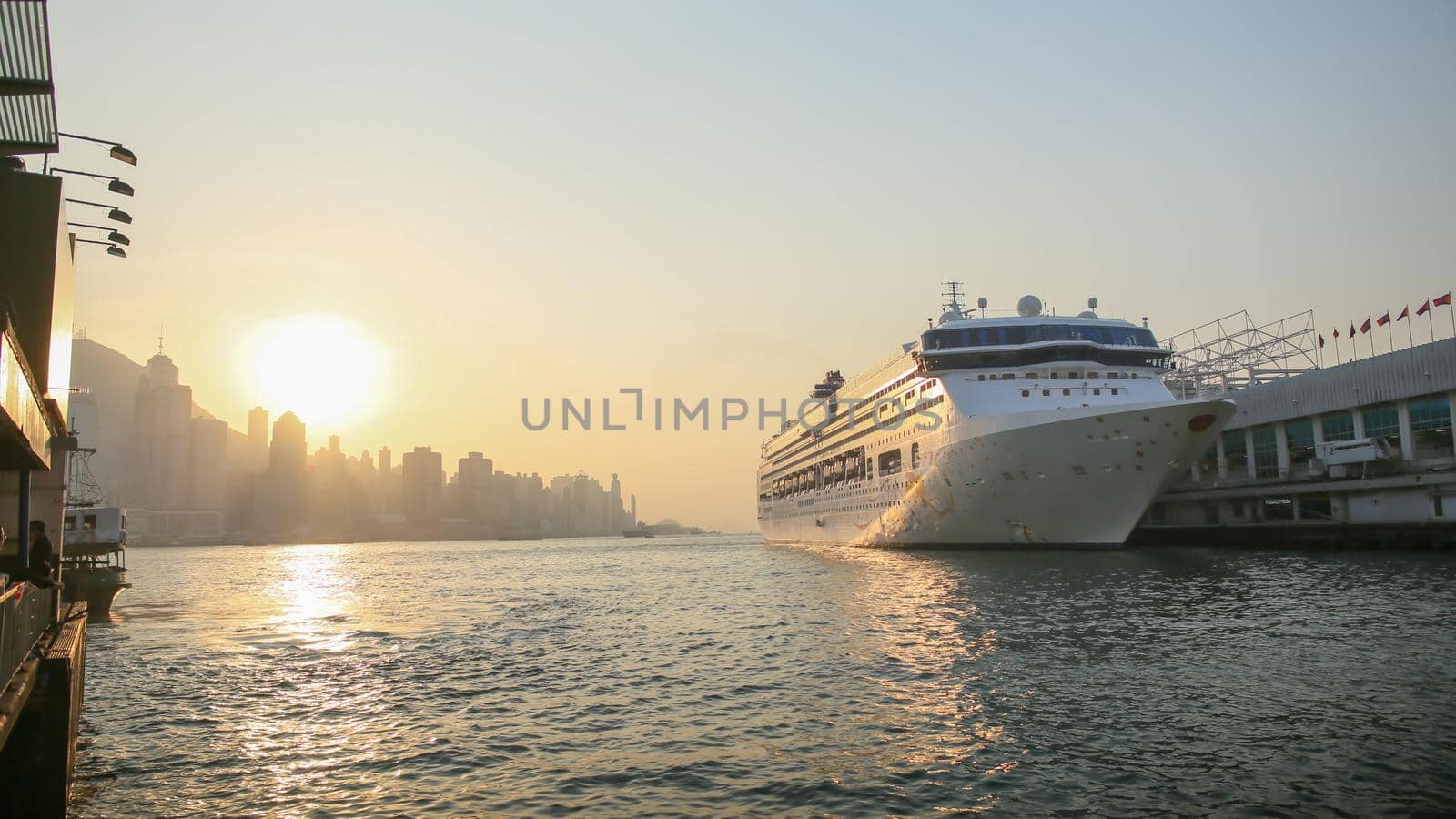 Cruise liner in Victoria harbor in the rays of sunset. View of the sea of Hong Kong and skyscrapers against the backdrop of the mountains