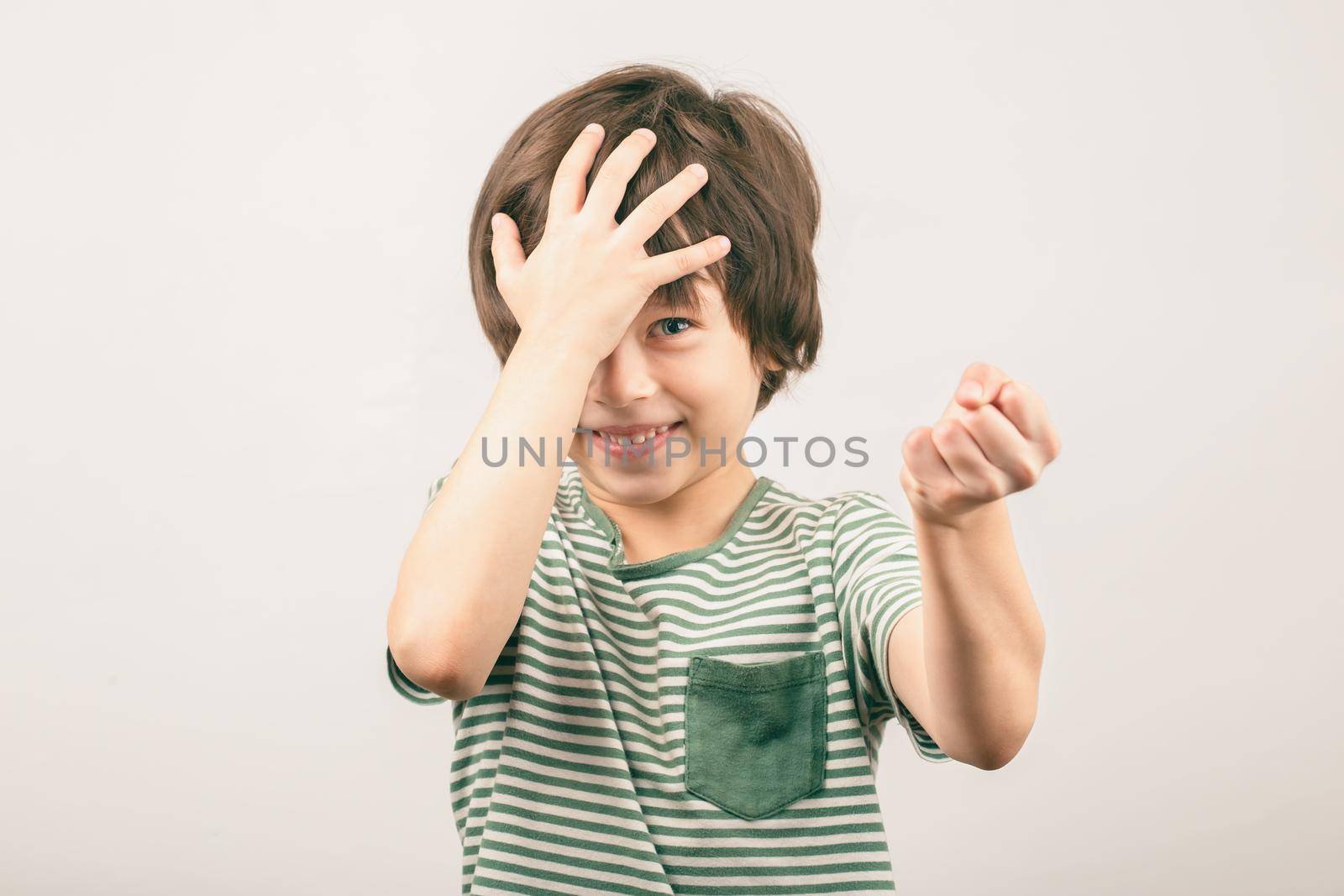 White 6 years old boy covering his head threatens the enemy with a fist looking to the camera. Kid quarreling and fighting. Child abuse concept