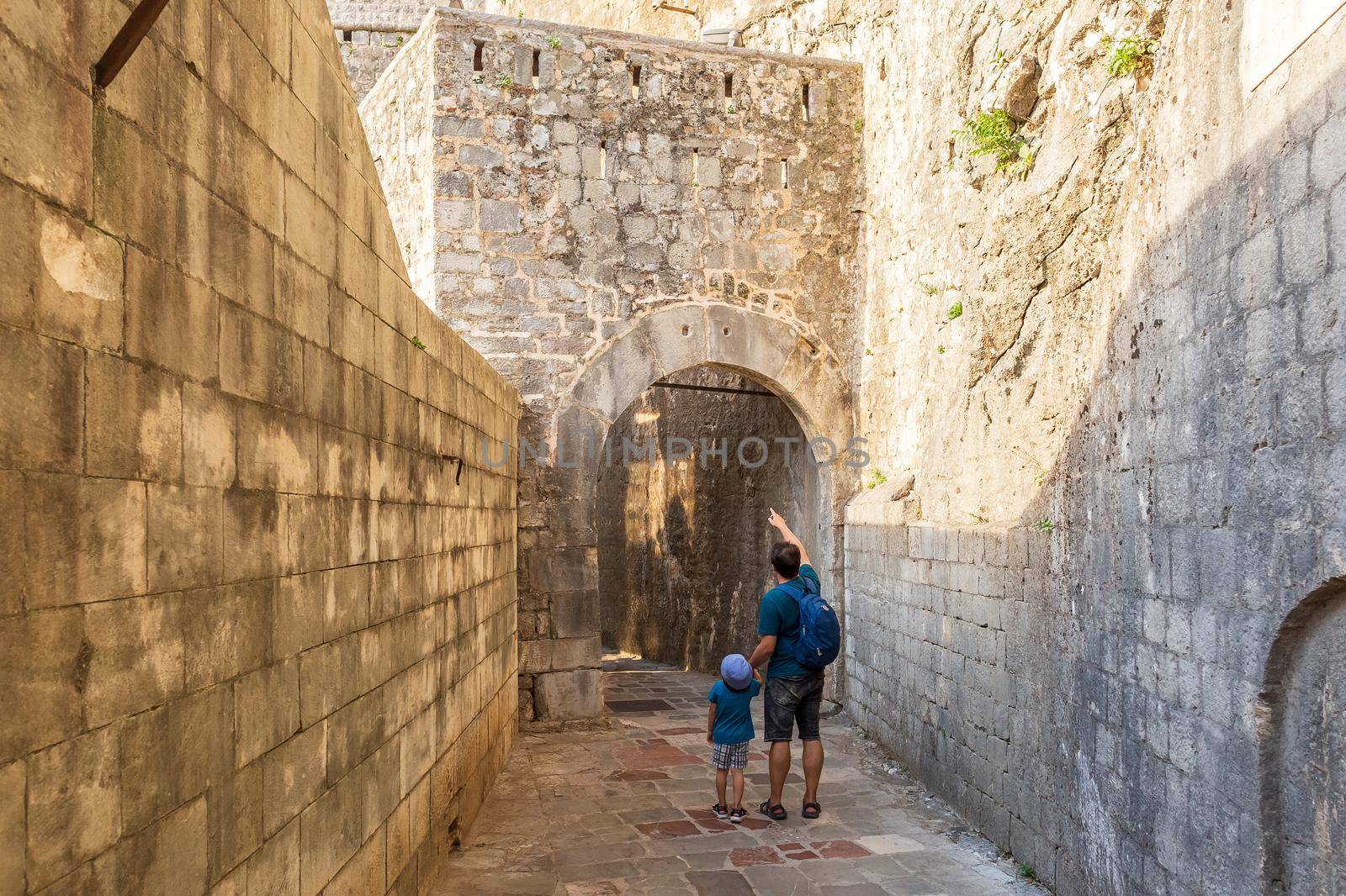 Father and son walking among medieval fortress walls in Kotor city, Montenegro. Tourists exploring narrow paved stone street in the old town on a summer sunny day.
