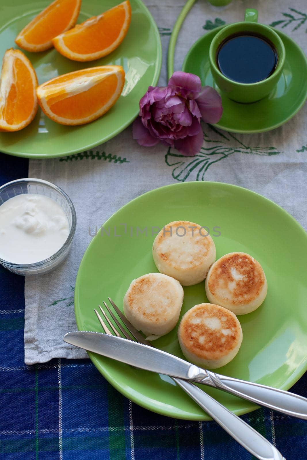 Delicious Dietary Cheesecakes from Homemade Farmer's Cheese for breakfast, black coffee in a green cup, chopped orange and
and purple tulip on a blue tablecloth