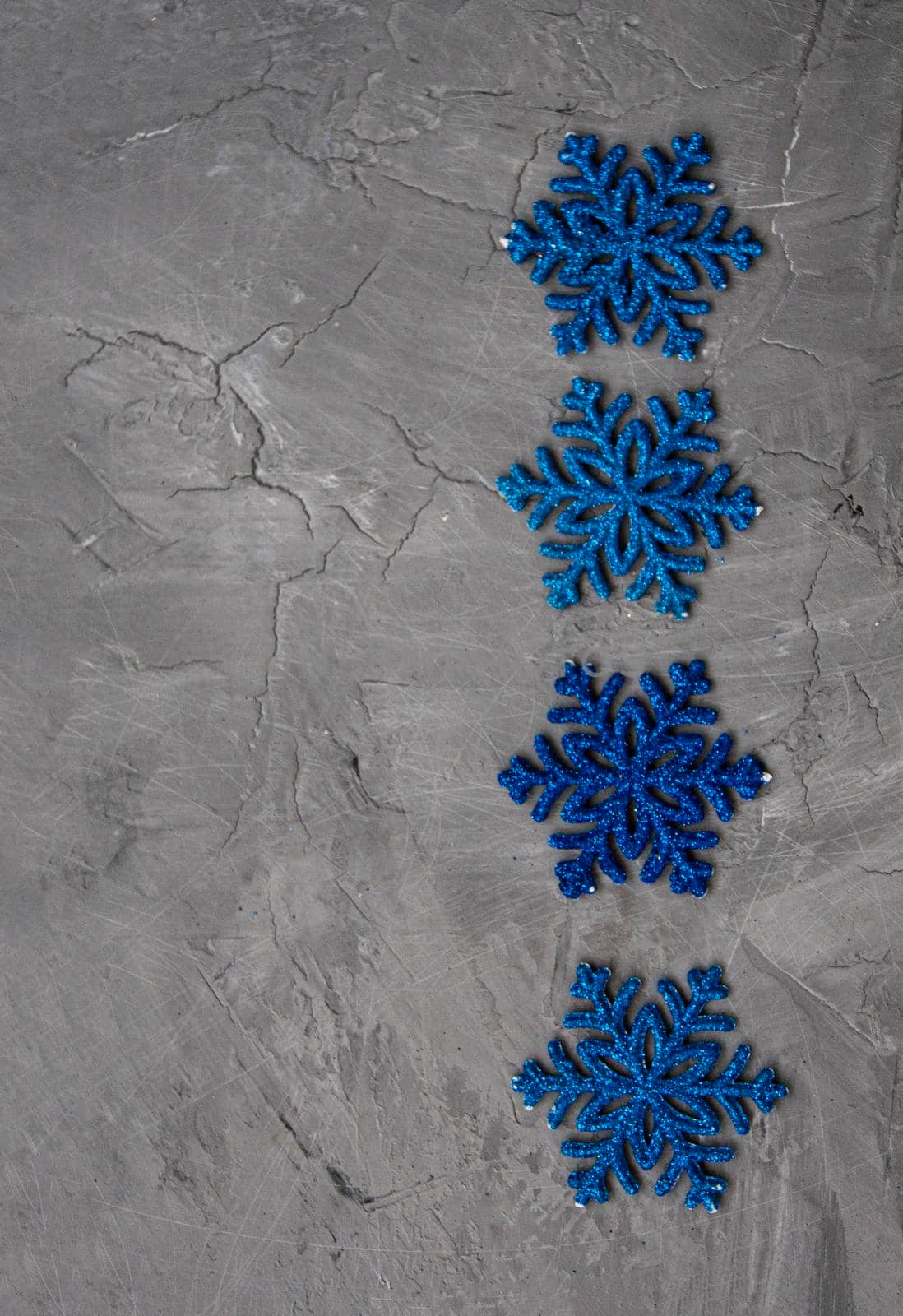 Many blue snowflakes lie in a row on a gray concrete background. There is a place for a welcome text.