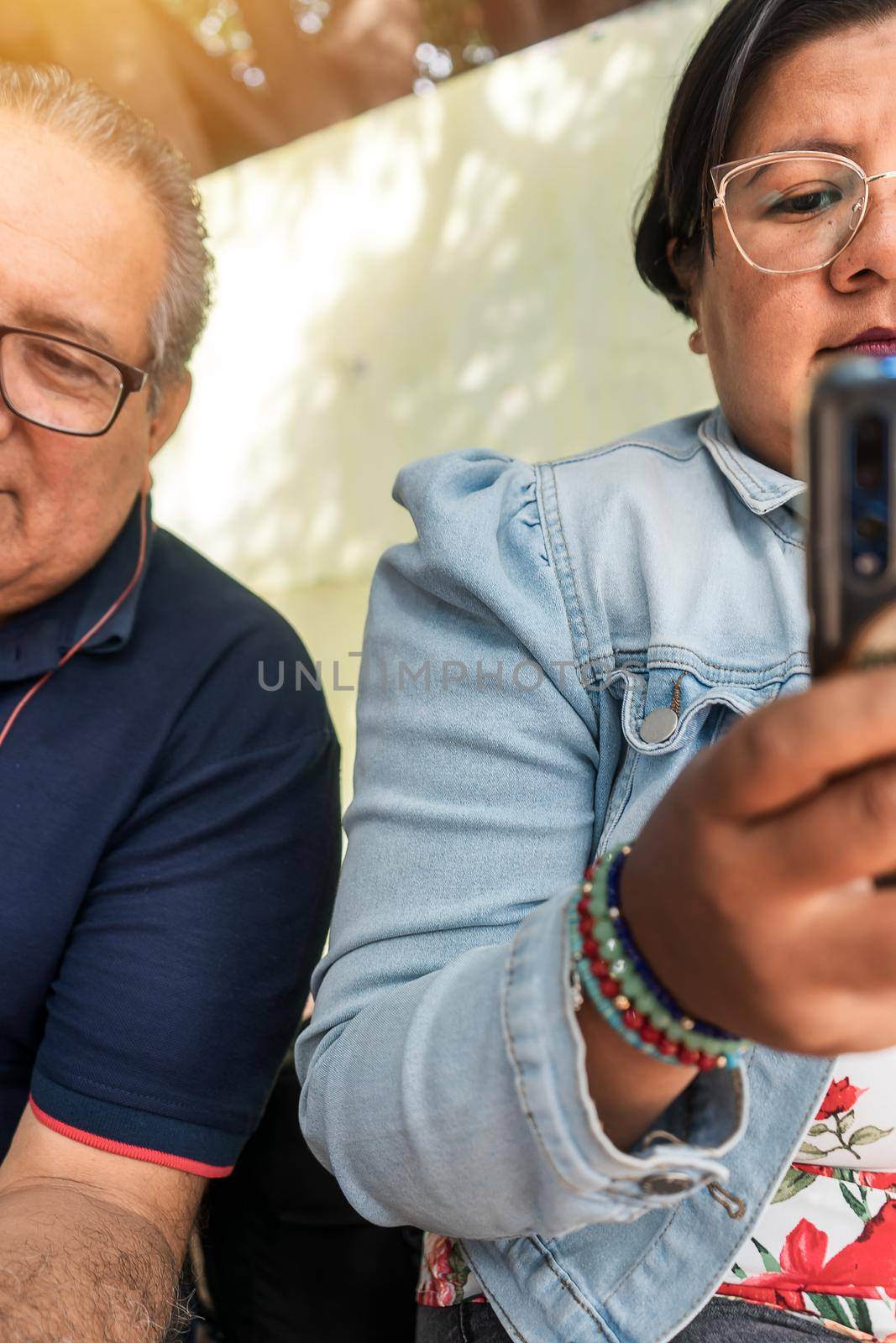 Vertical photo of a Latin mature man and a young brunette woman checking the cell phone outdoors