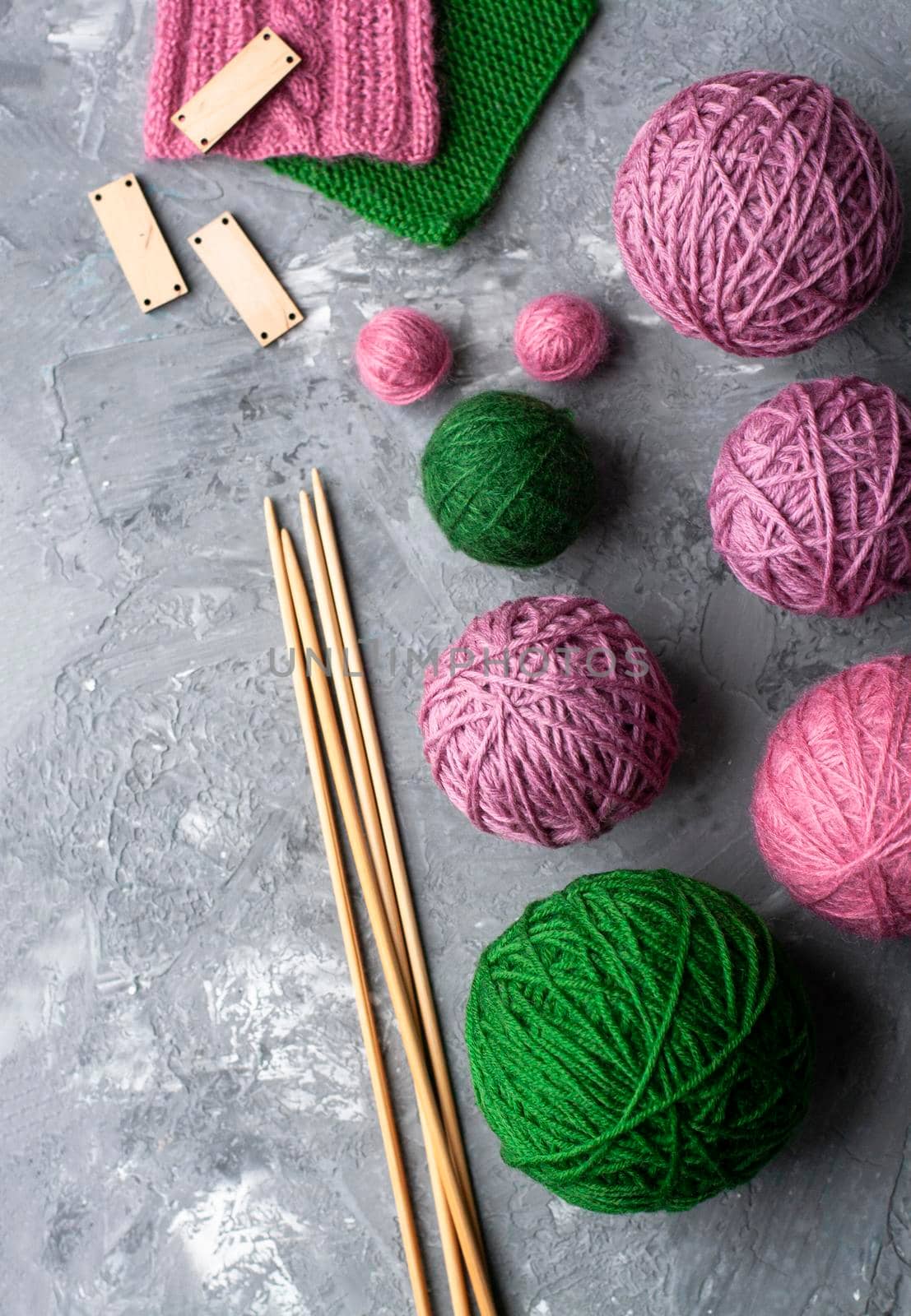 Samples of green and purple patterns, large balls of green and purple colors and wooden needles on a gray textured concrete background. Place for text.