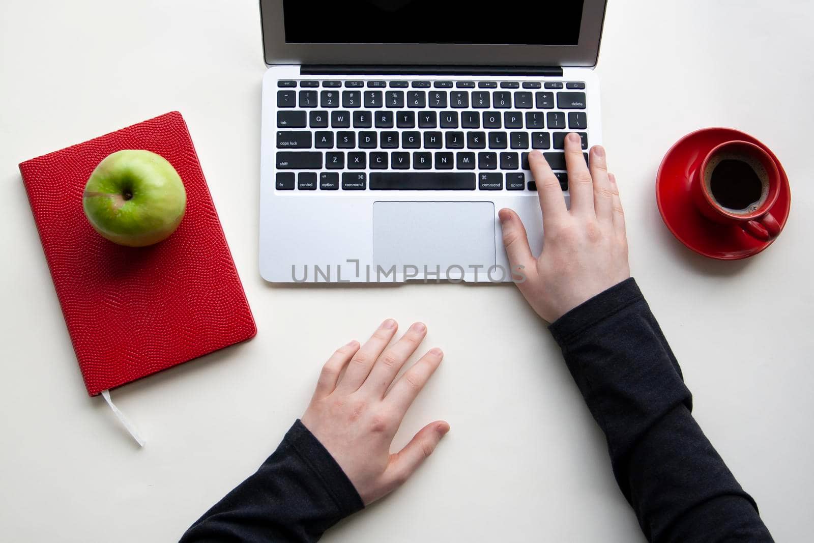 Man hands on wireless keyboard with red notebook, green apple and red cup of coffee on white table