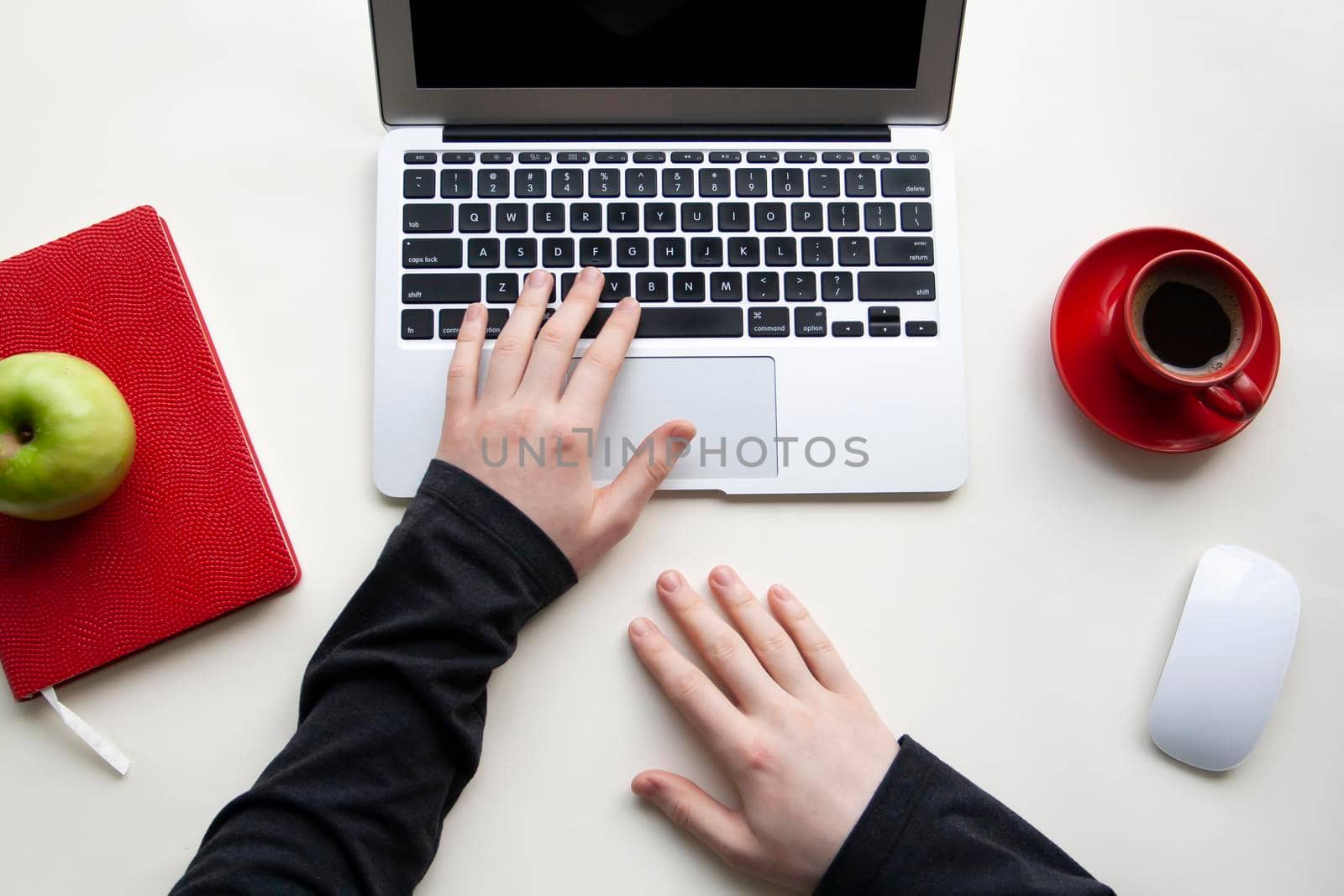 Man hands on wireless keyboard with red notebook, green apple and red cup of coffee on white table