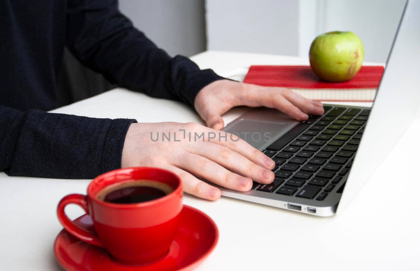 Man hands on wireless keyboard with red notebook, green apple and red cup of coffee on white table