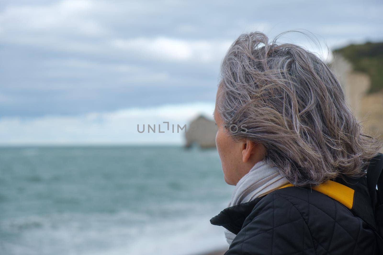 Portrait profile view of older woman with a scarf, backpack on cold beach. High quality photo