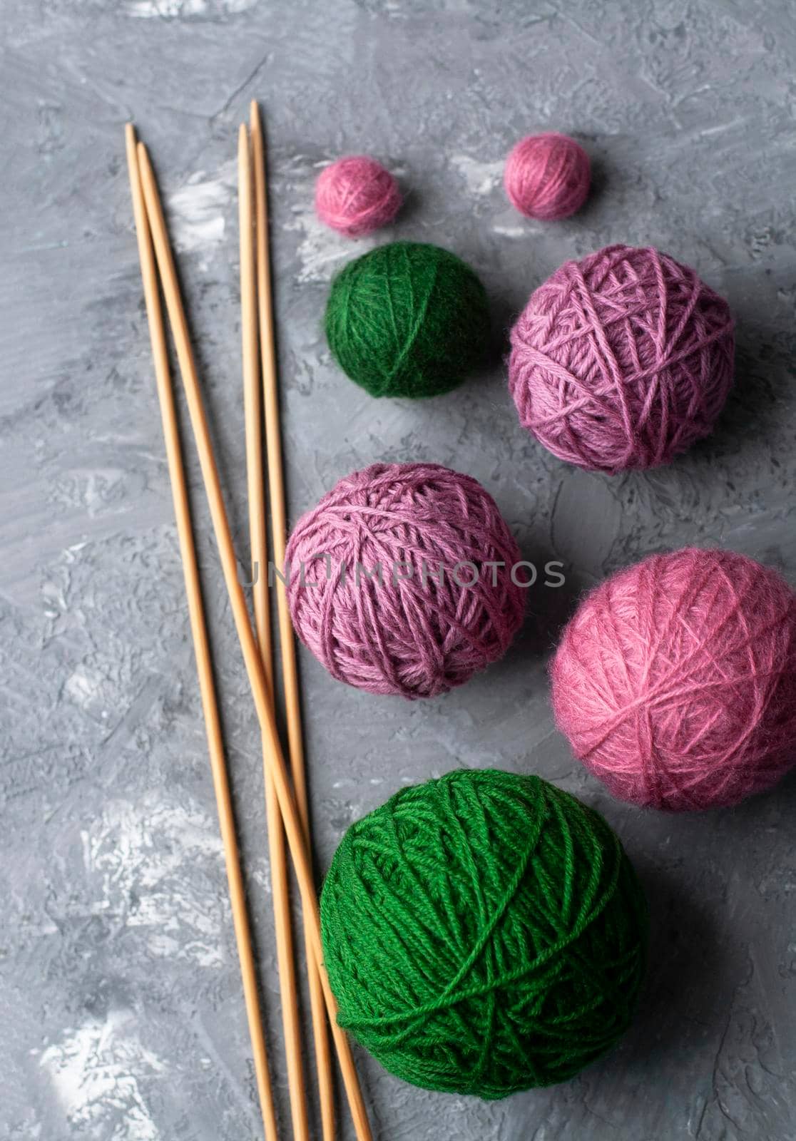 Samples of green and purple patterns, large balls of green and purple colors and wooden needles on a gray textured concrete background. Place for text.