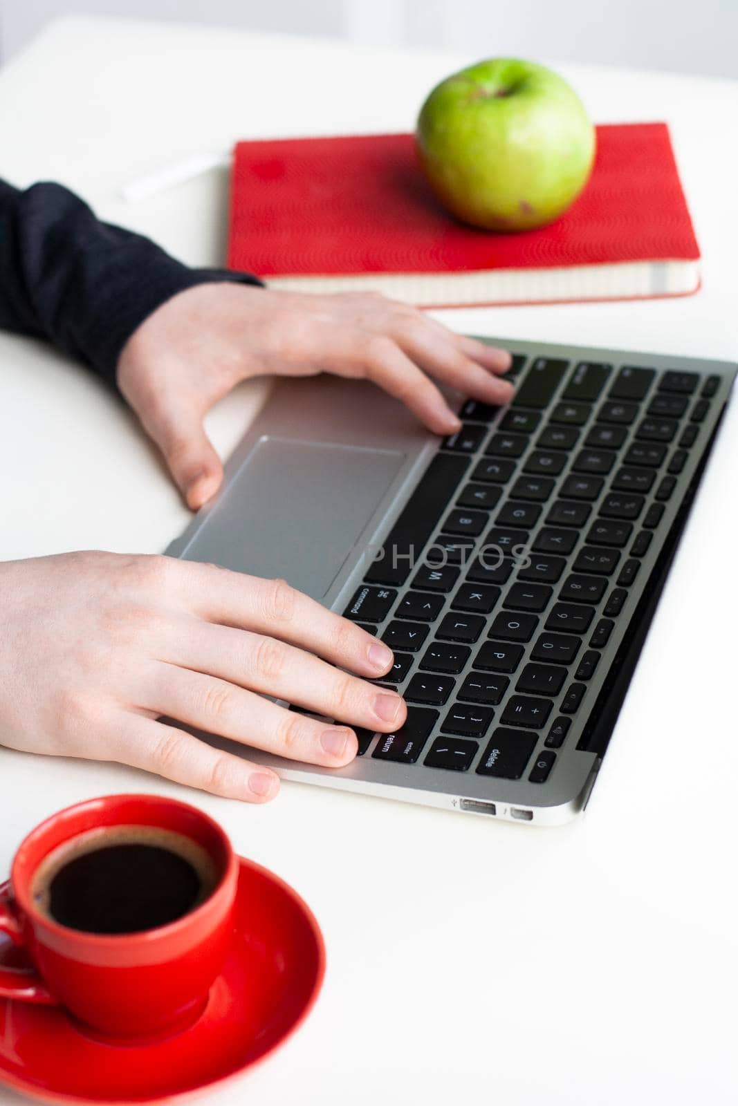 Man hands on wireless keyboard with red notebook, green apple and red cup of coffee on white table
