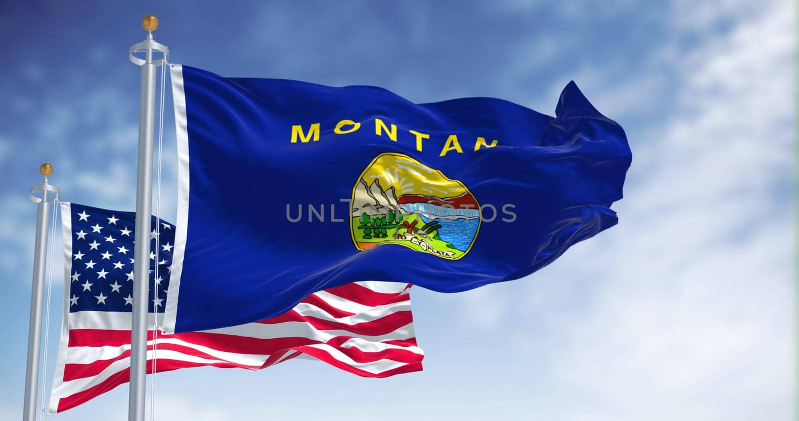 The Montana state flag waving along with the national flag of the United States of America. In the background there is a clear sky. Montana is a state in the western United States
