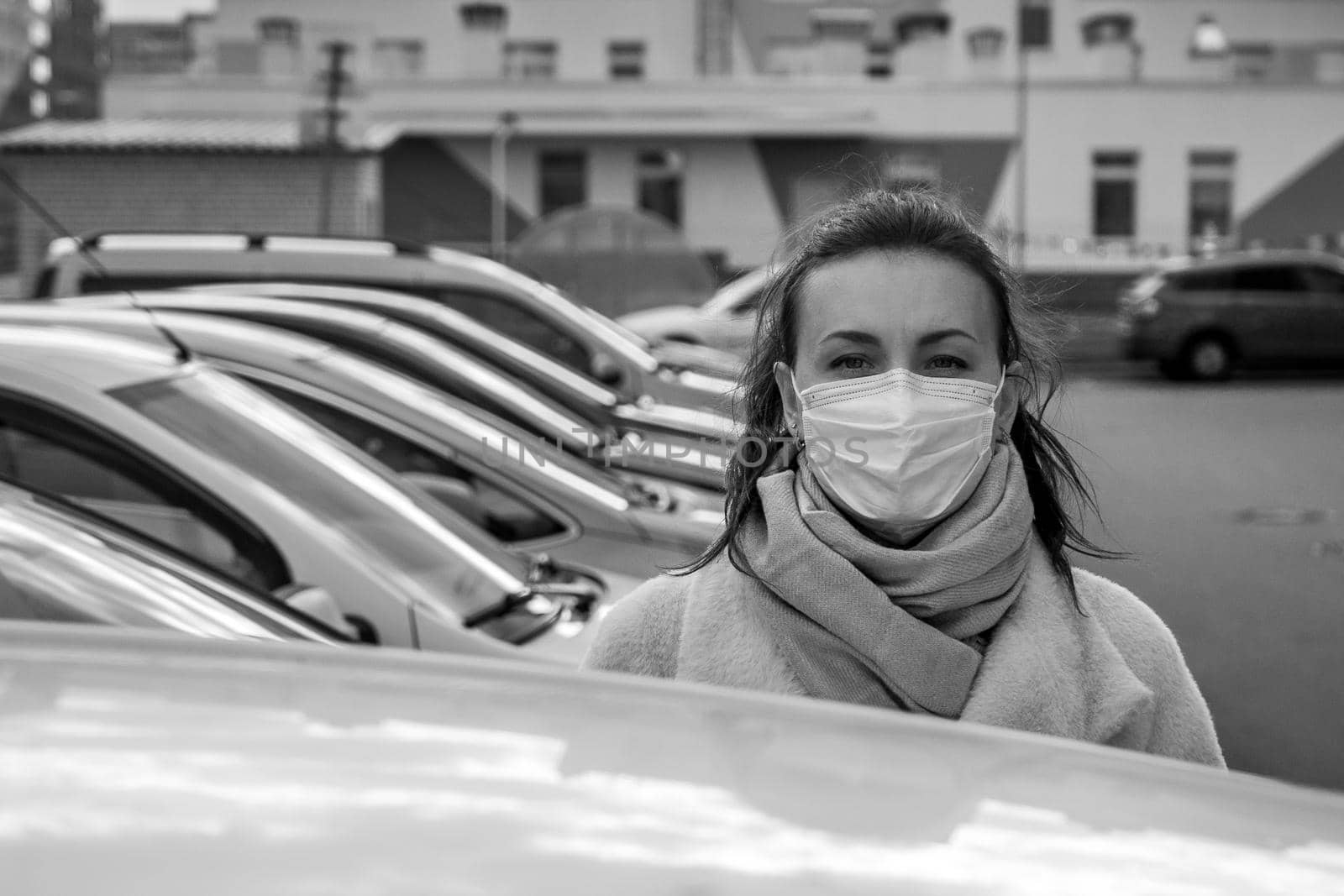 picture of a girl in a mask, on the street. Against the background of parked cars. isolated Covid-19 pandemic.