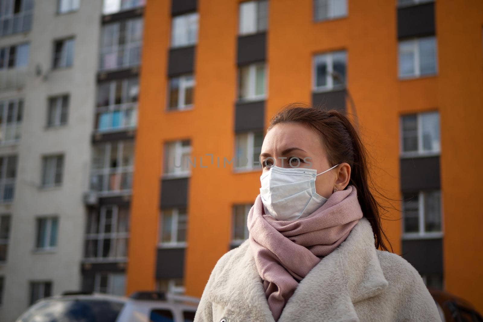 Shot of a girl in wearing face mask for protection, on the street. Against the background of a residential building with windows. lockdown Covid-19 pandemic.