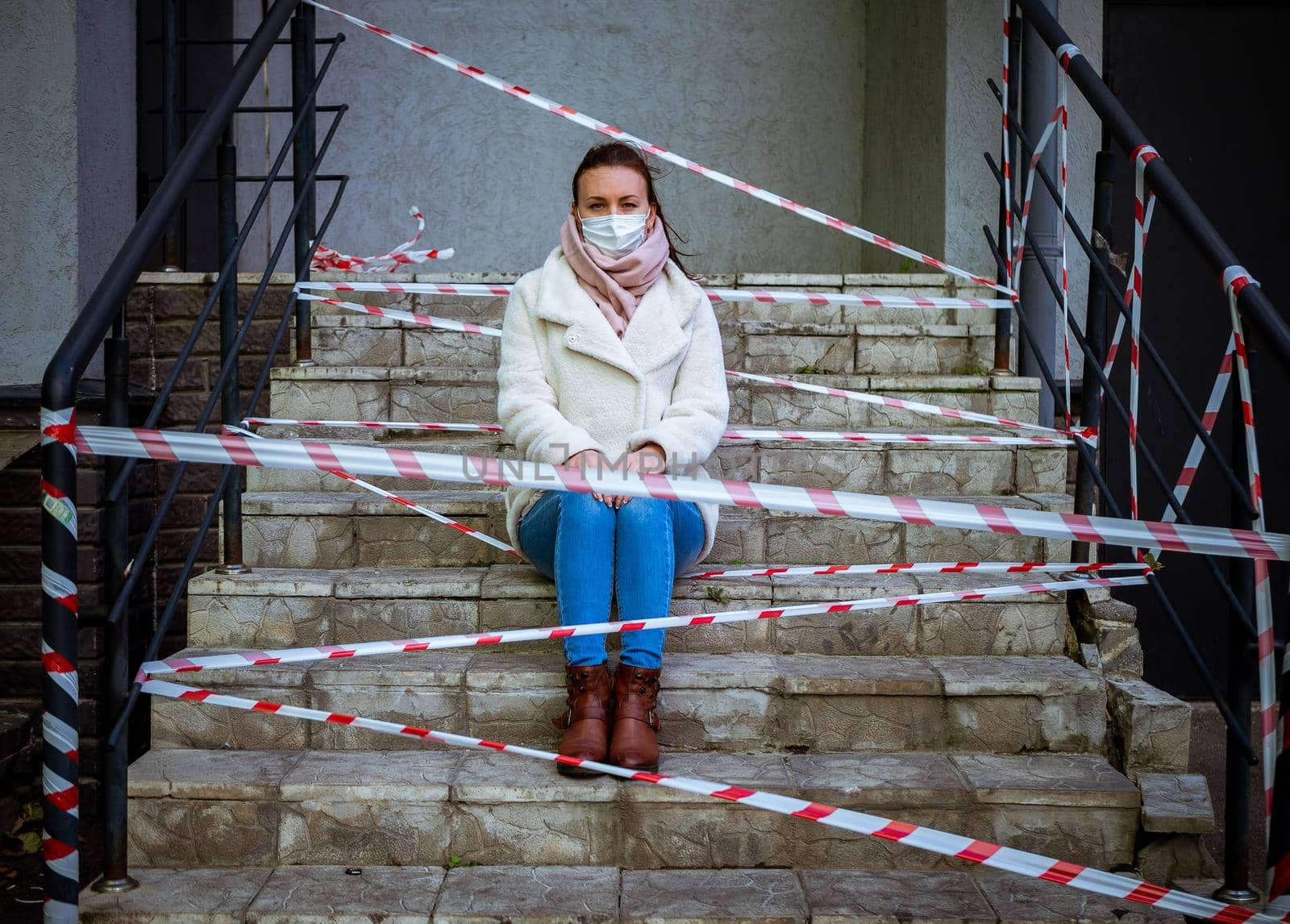 Photo of a girl in a mask. Sitting on the street with danger warning tapes. isolated Covid-19 pandemic.