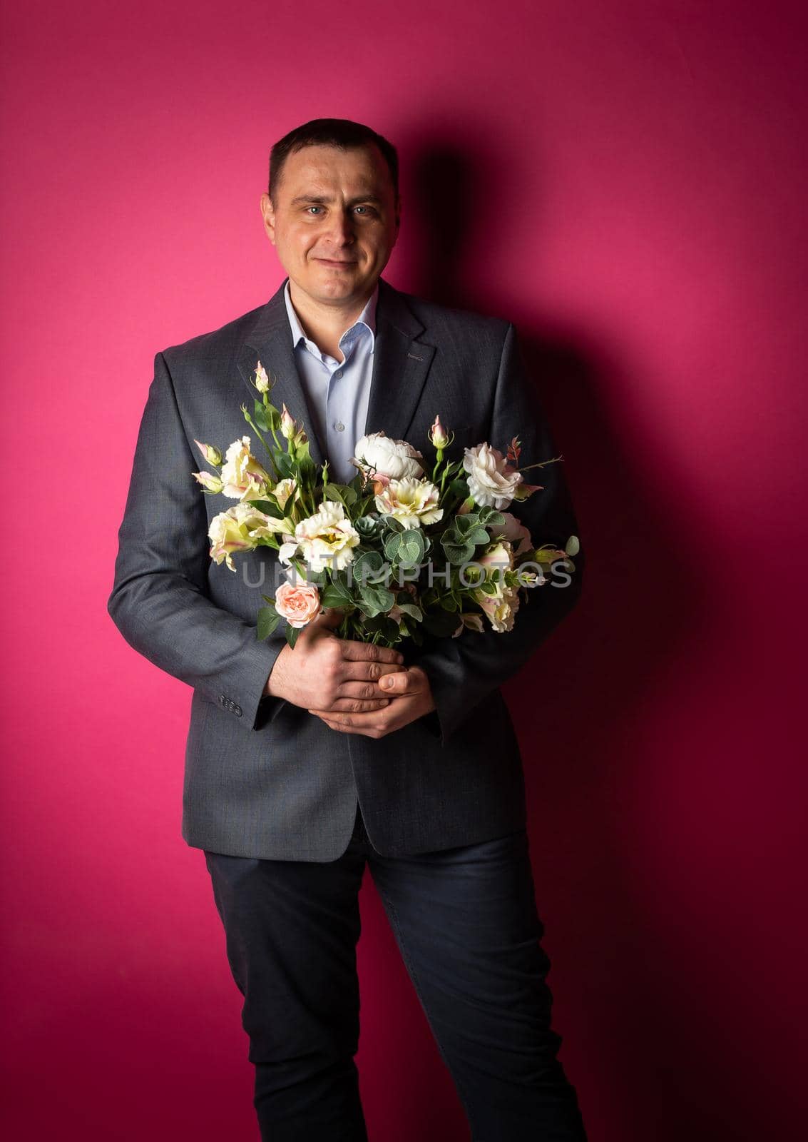 handsome businessman in a suit looks at the camera with a bouquet of flowers. isolated on a pink background