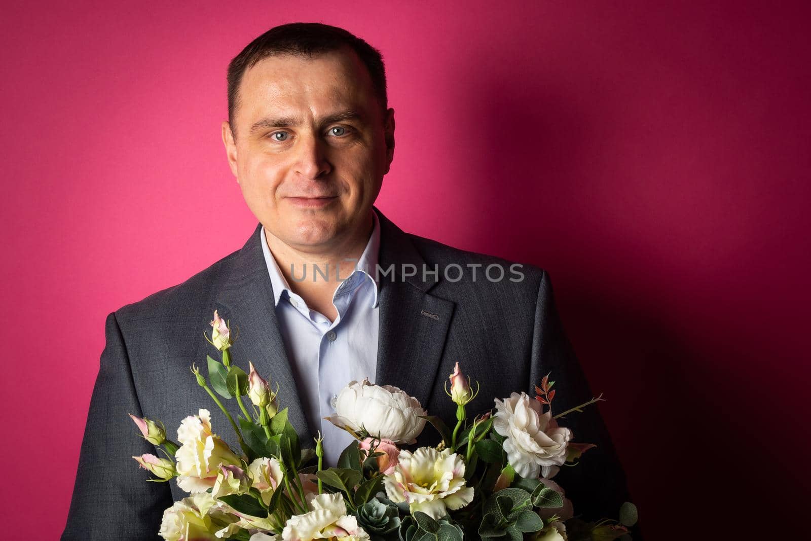 handsome businessman in a suit looks at the camera with a bouquet of flowers. isolated on a pink background