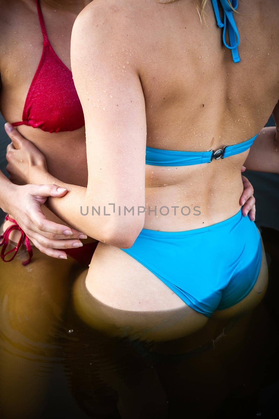 Side view of two young women with beautiful bodies in bikinis. Blue and pink swimsuit in the water.