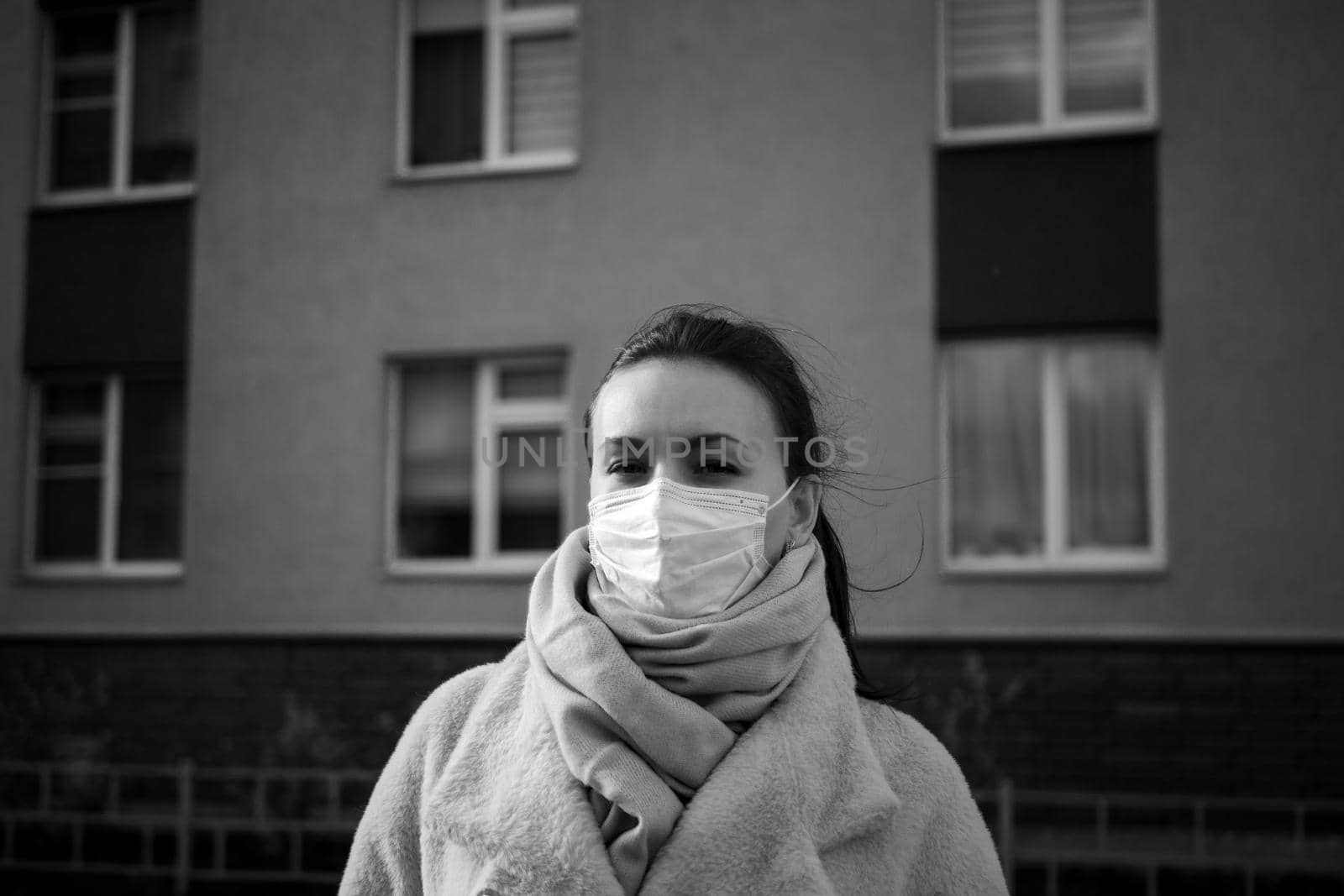 Shot of a girl in wearing face mask for protection, on the street. Against the background of a residential building with windows. lockdown Covid-19 pandemic.