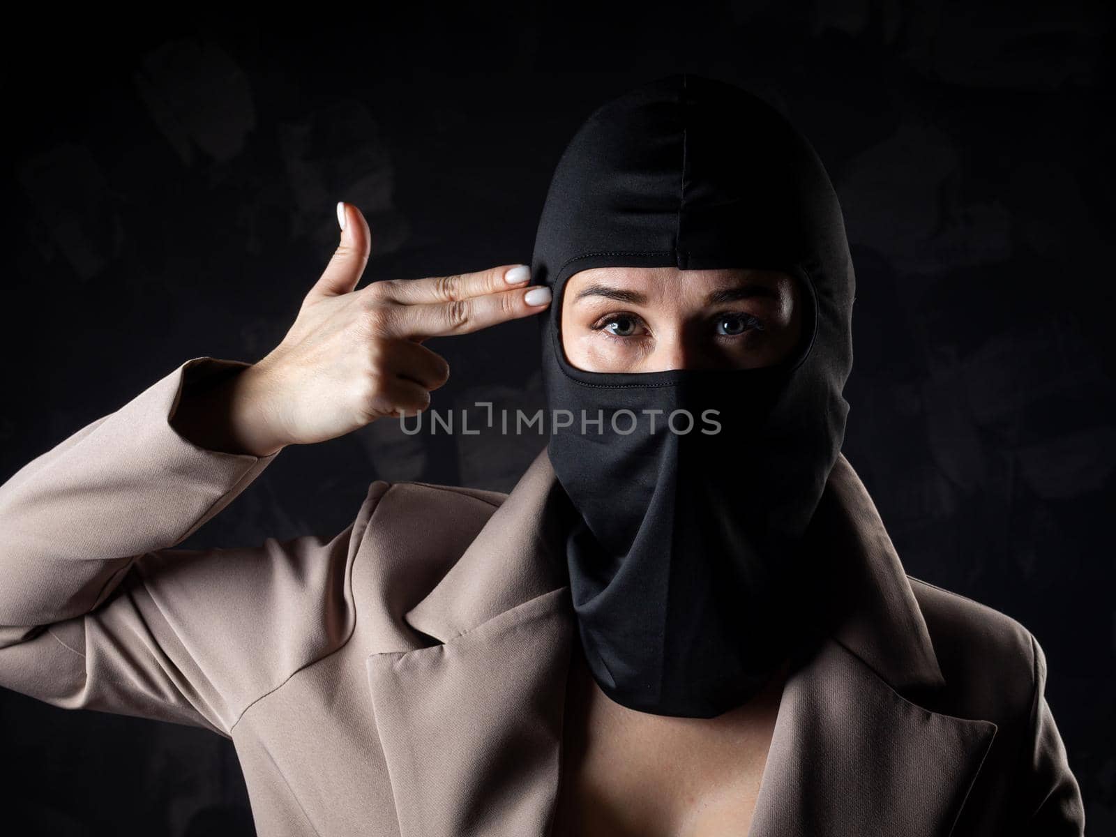 Portrait of a girl in a black balaclava and beige coat. Shot in the studio on a dark background.