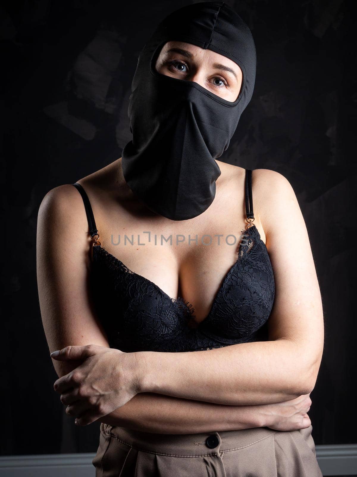 Portrait of a girl in a black balaclava and a black bra. Shot in the studio on a dark background.