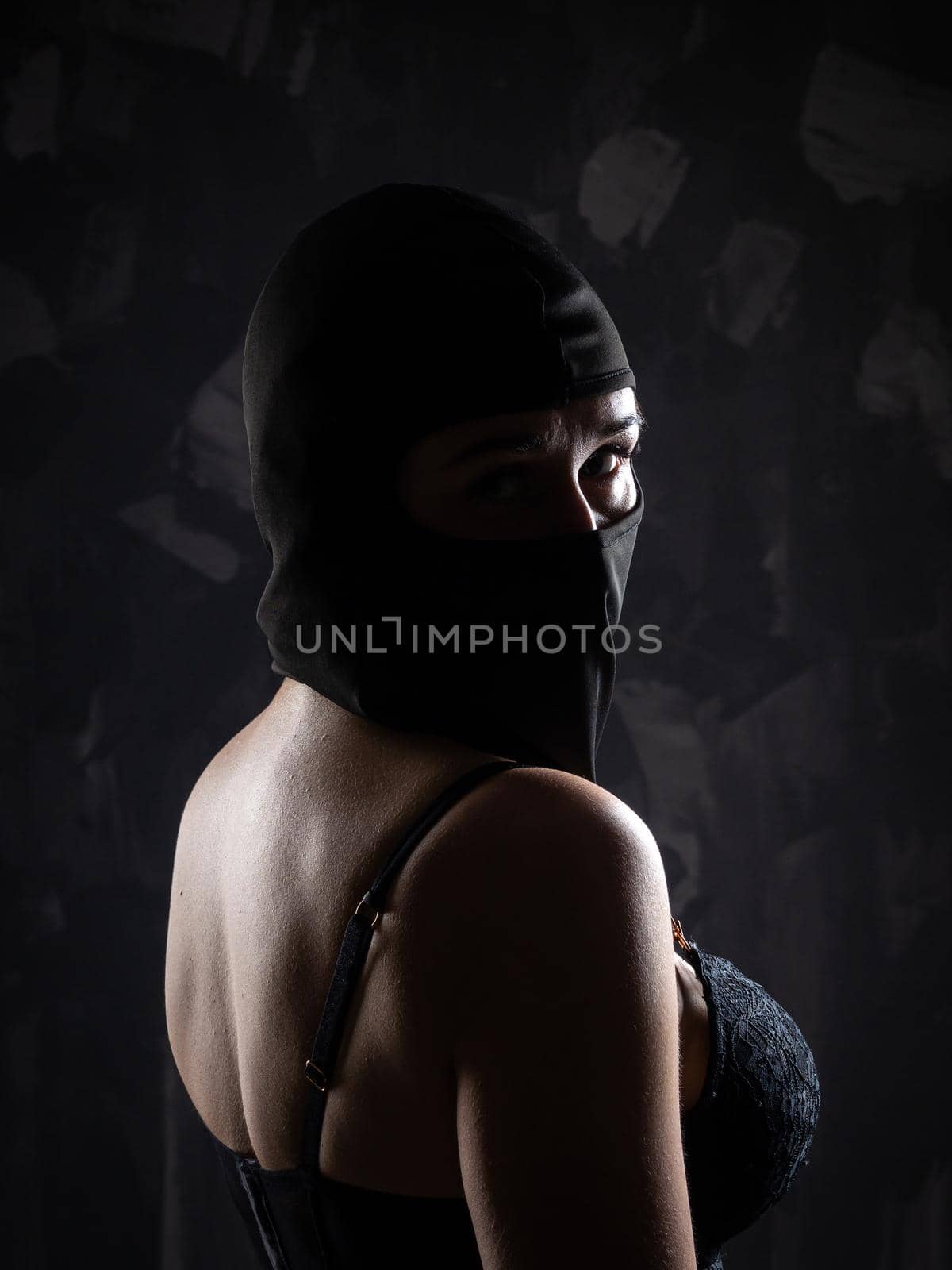 Portrait of a girl in a black balaclava and a black bra. Shot in the studio on a dark background.