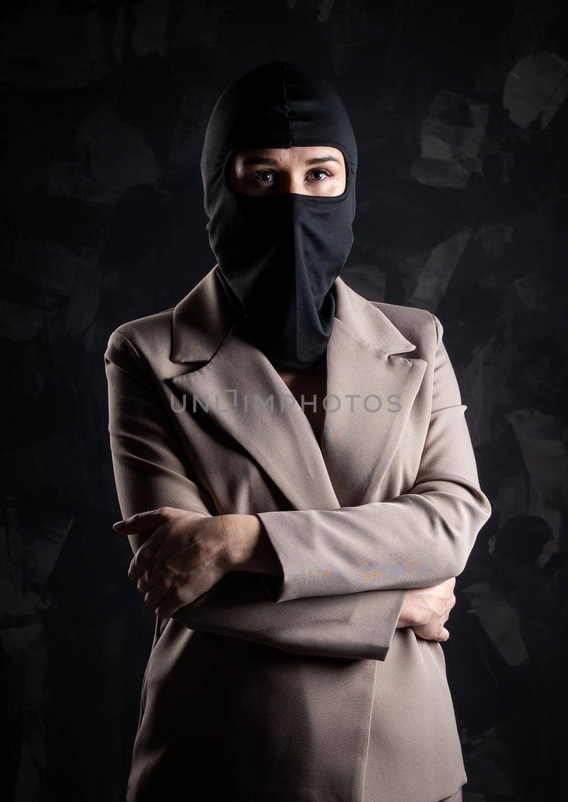 Portrait of a girl in a black balaclava and beige coat. Shot in the studio on a dark background.