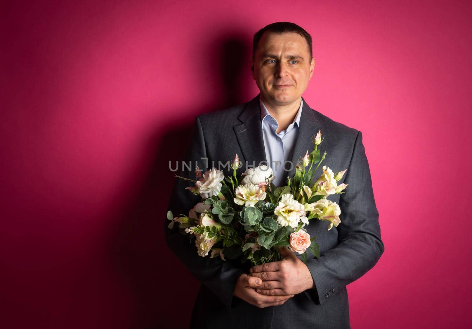 handsome businessman in a suit looks at the camera with a bouquet of flowers. isolated on a pink background