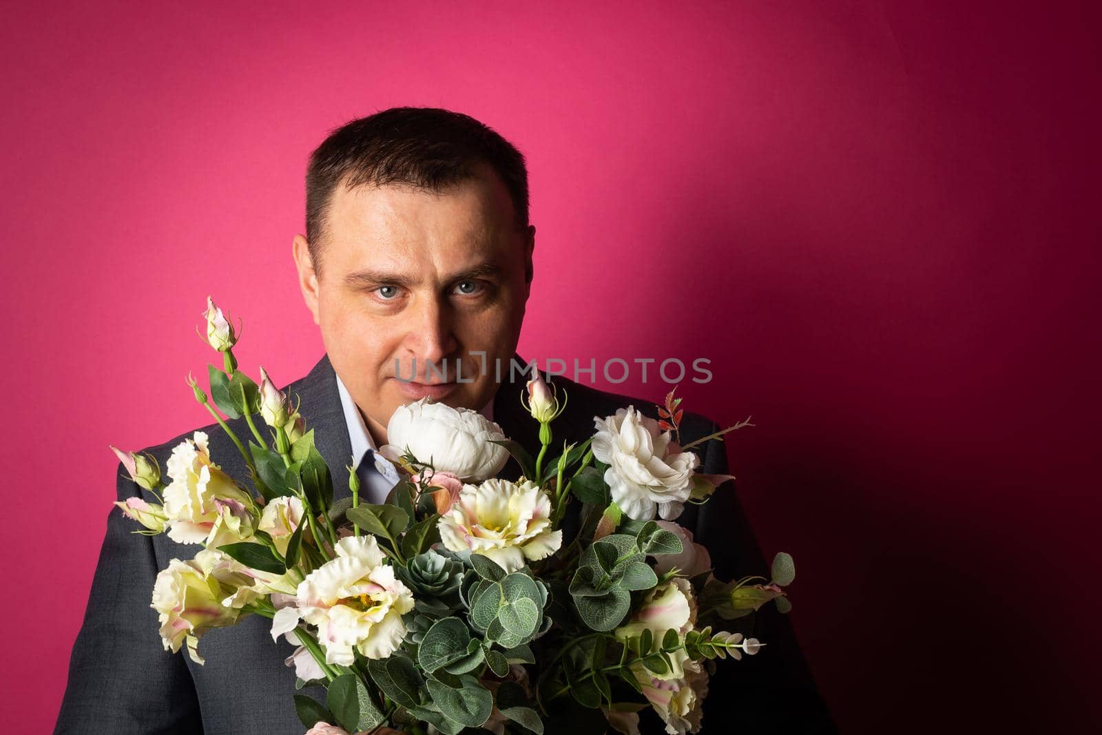 handsome businessman in a suit looks at the camera with a bouquet of flowers. isolated on a pink background