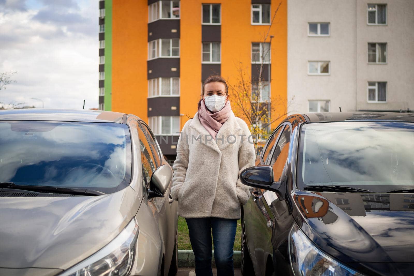 picture of a girl in a mask, on the street. Against the background of parked cars. isolated Covid-19 pandemic.