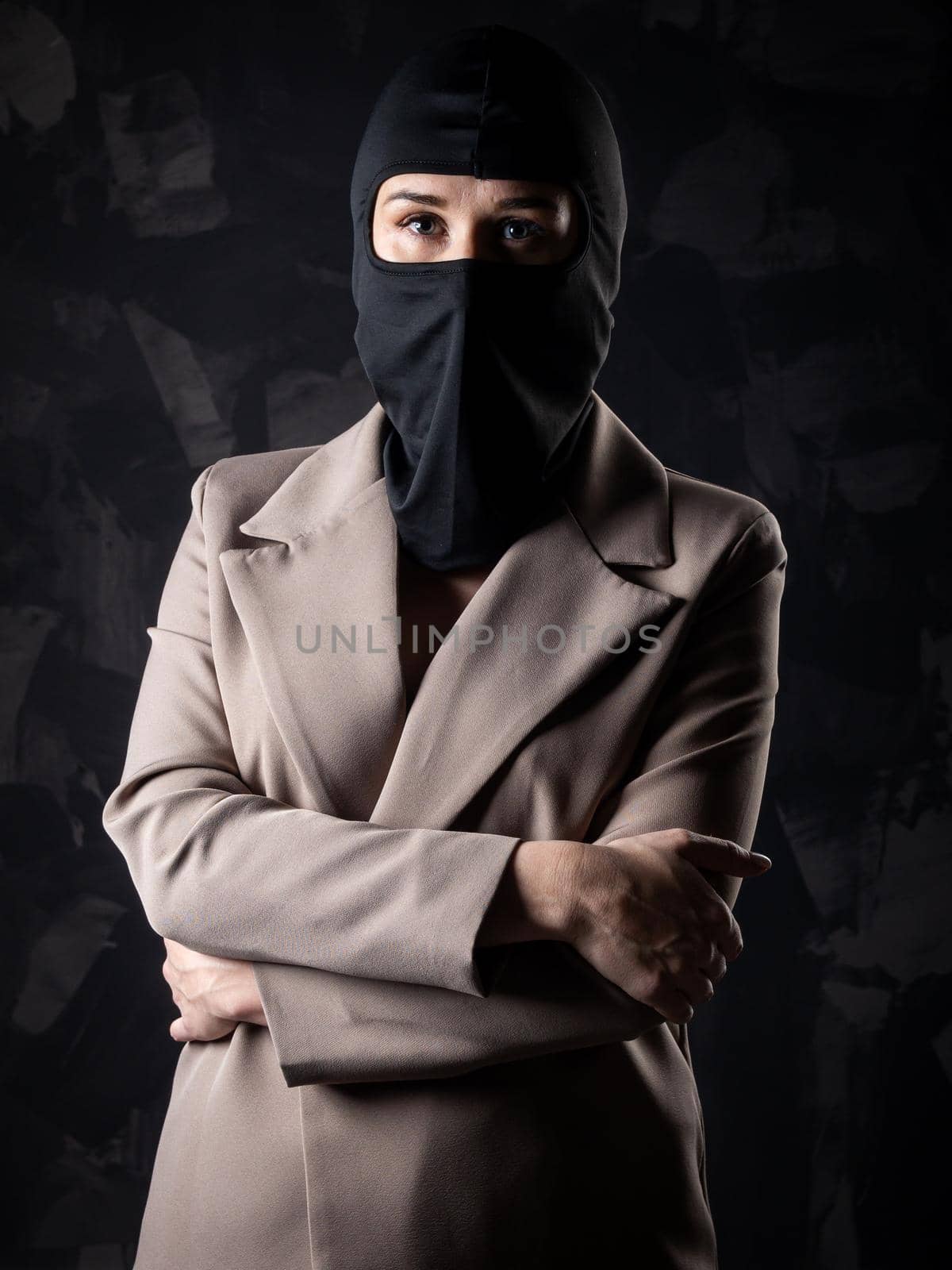 Portrait of a girl in a black balaclava and beige coat. Shot in the studio on a dark background.