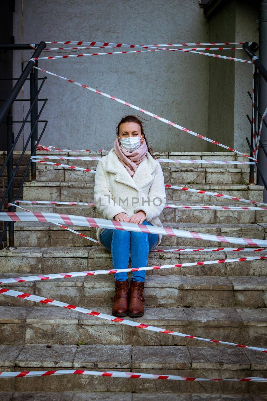 Photo of a girl in a mask. Sitting on the street with danger warning tapes. isolated Covid-19 pandemic.