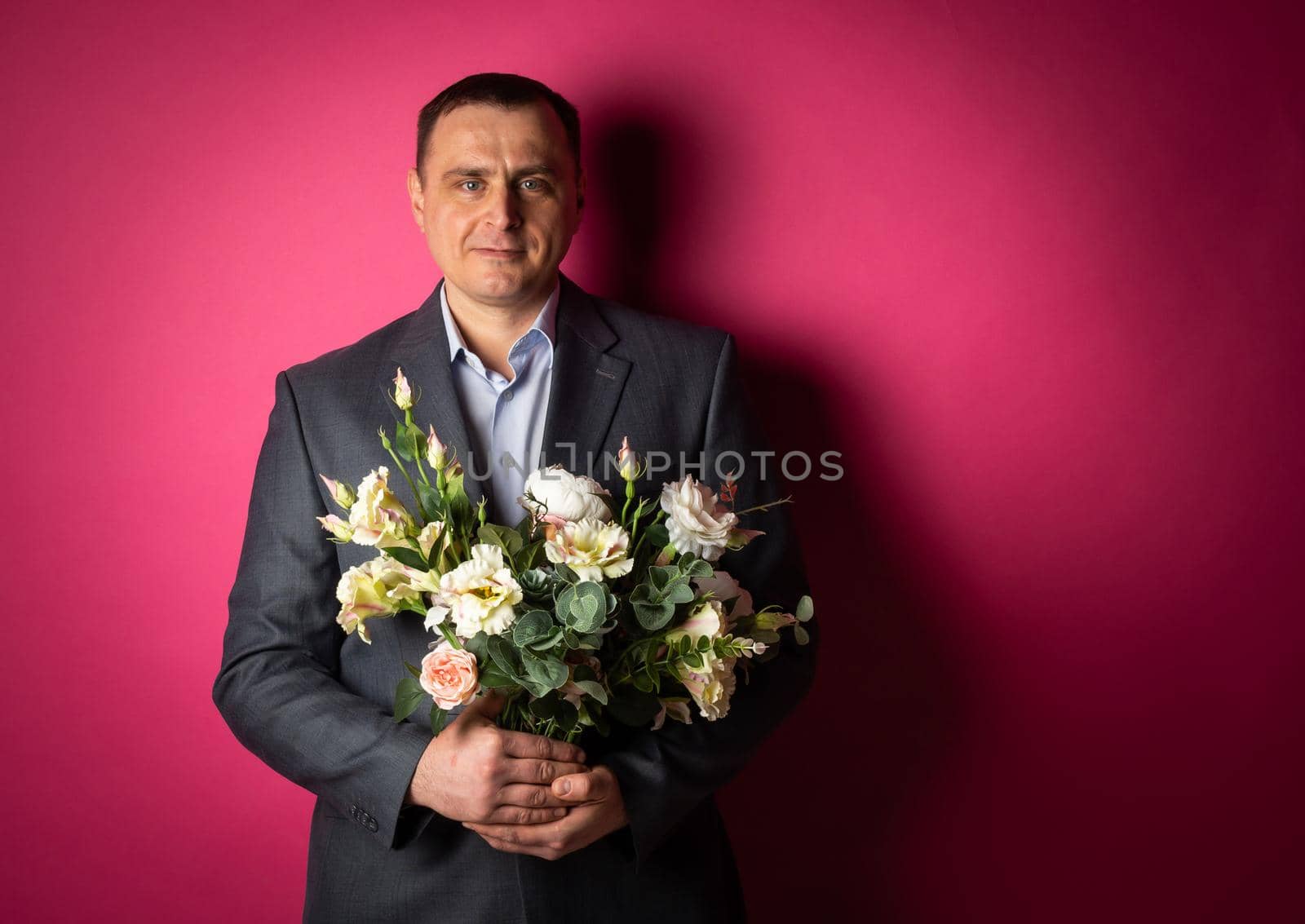 handsome businessman in a suit looks at the camera with a bouquet of flowers. isolated on a pink background