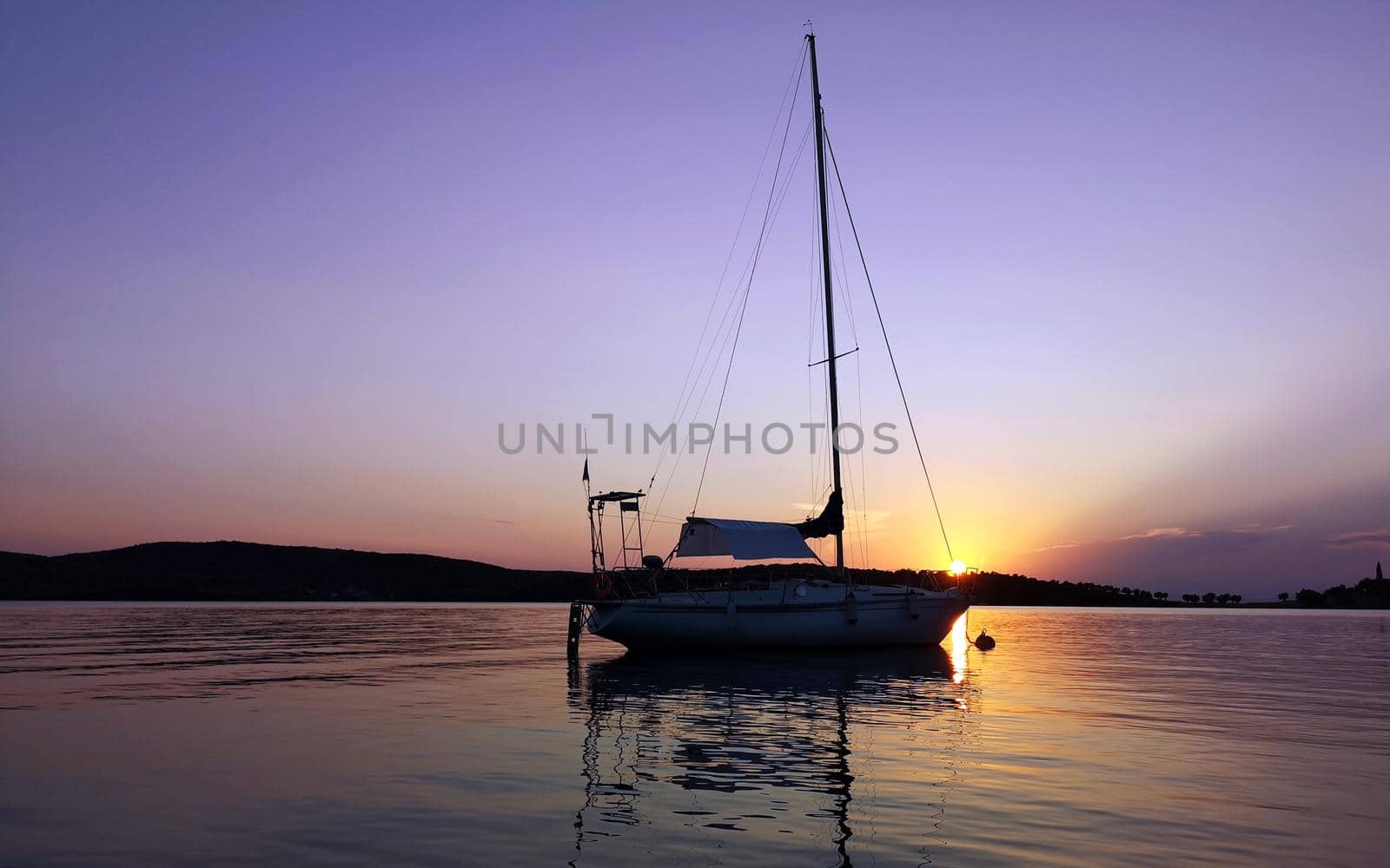 A sailboat anchored in a bay on a beautiful sunset in Greece