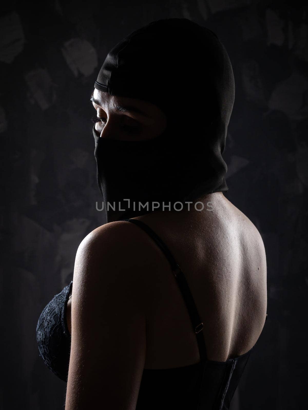 Portrait of a girl in a black balaclava and a black bra. Shot in the studio on a dark background.