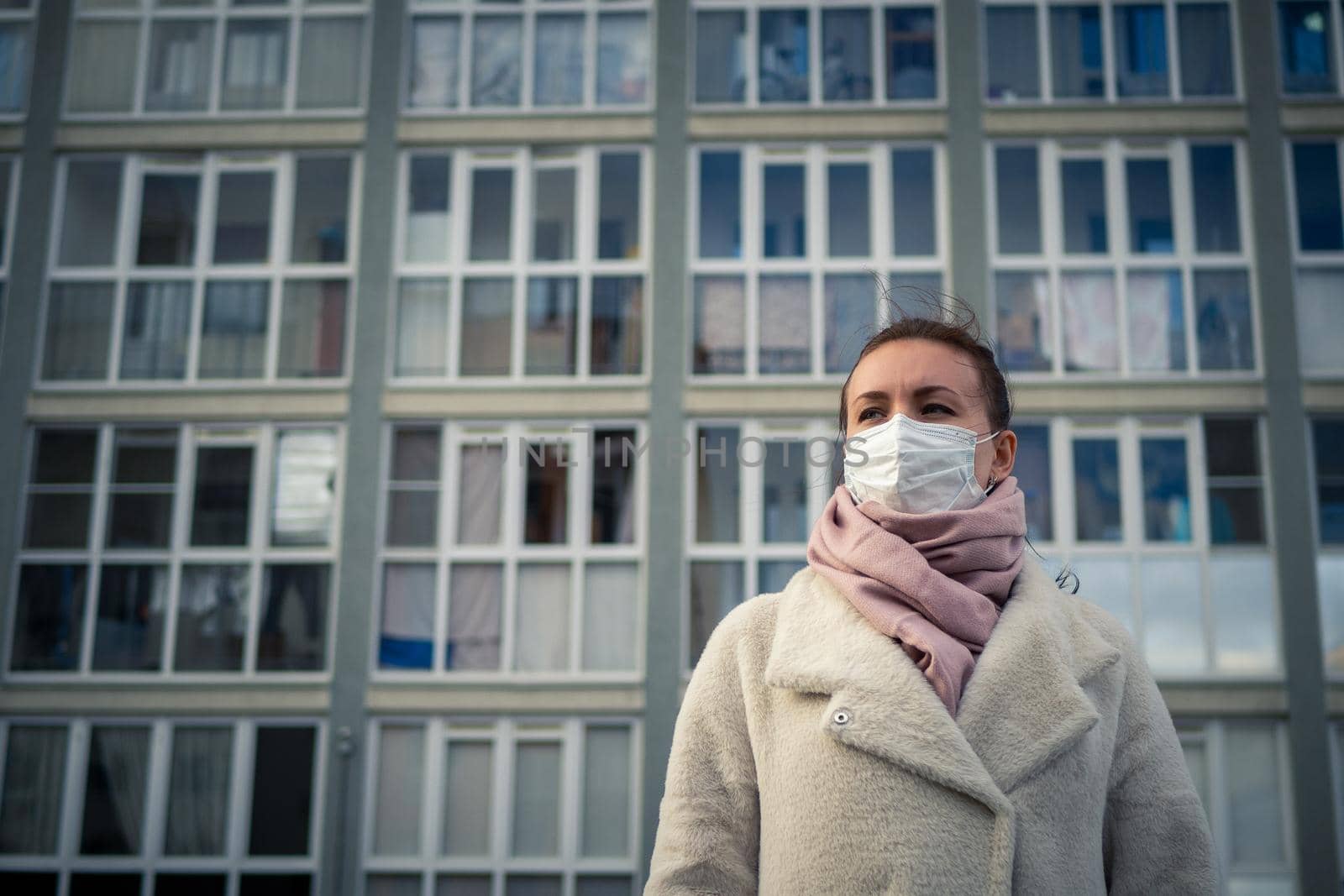 Shot of a girl in wearing face mask for protection, on the street. Against the background of a residential building with windows. lockdown Covid-19 pandemic.