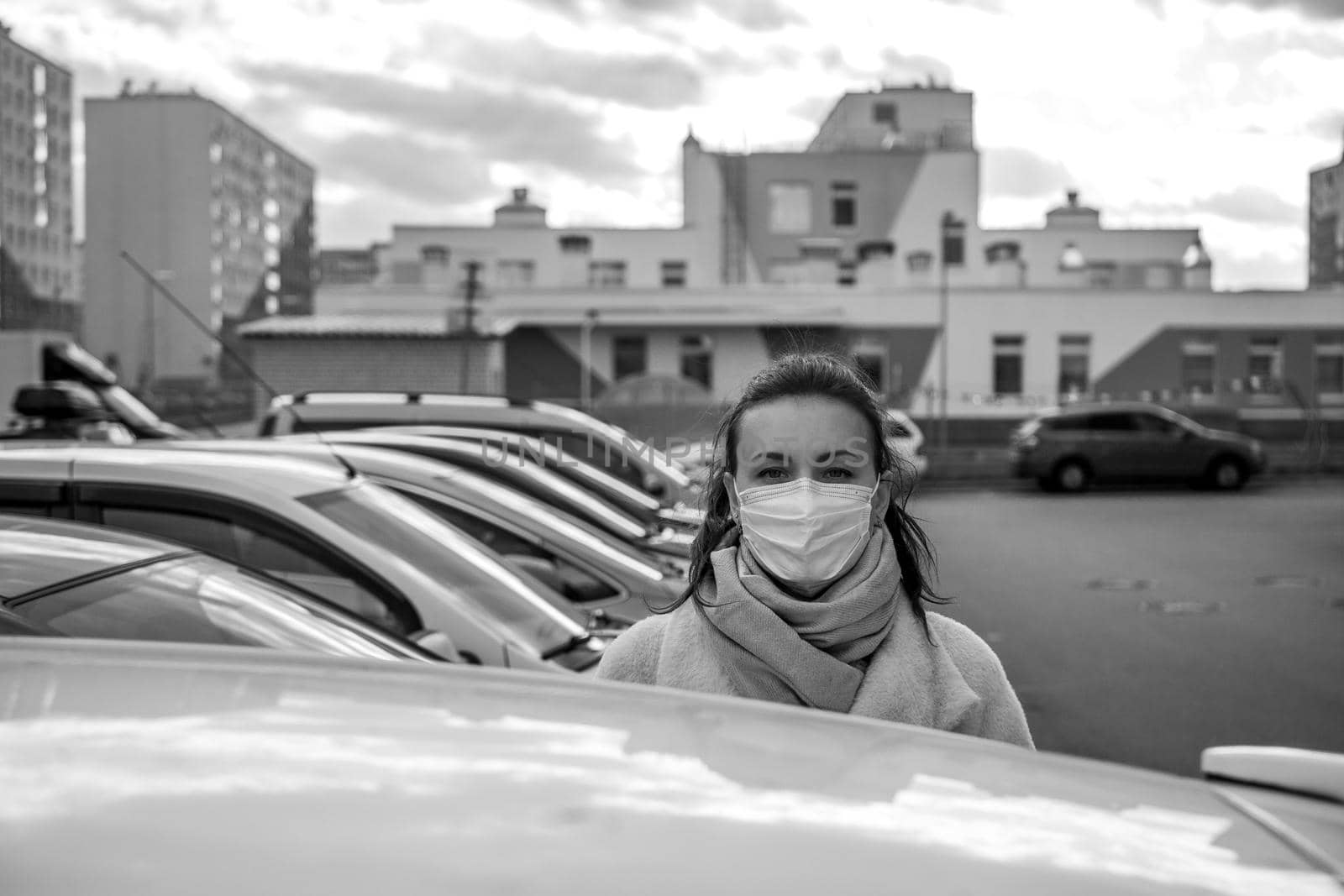 picture of a girl in a mask, on the street. Against the background of parked cars. isolated Covid-19 pandemic.