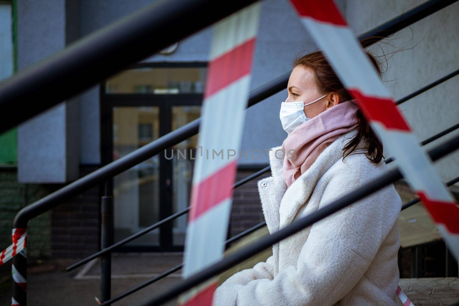 Photo of a girl in a mask. Sitting on the street with danger warning tapes. isolated Covid-19 pandemic.