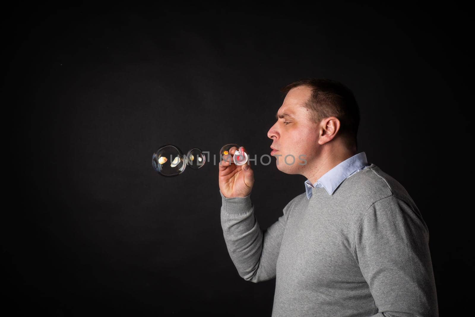 handsome man in a suit is blowing soap bubbles. isolated on a black background