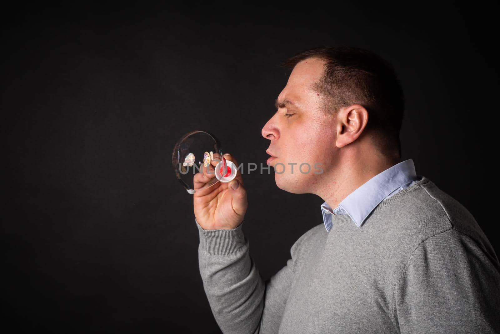 handsome man in a suit is blowing soap bubbles. isolated on a black background