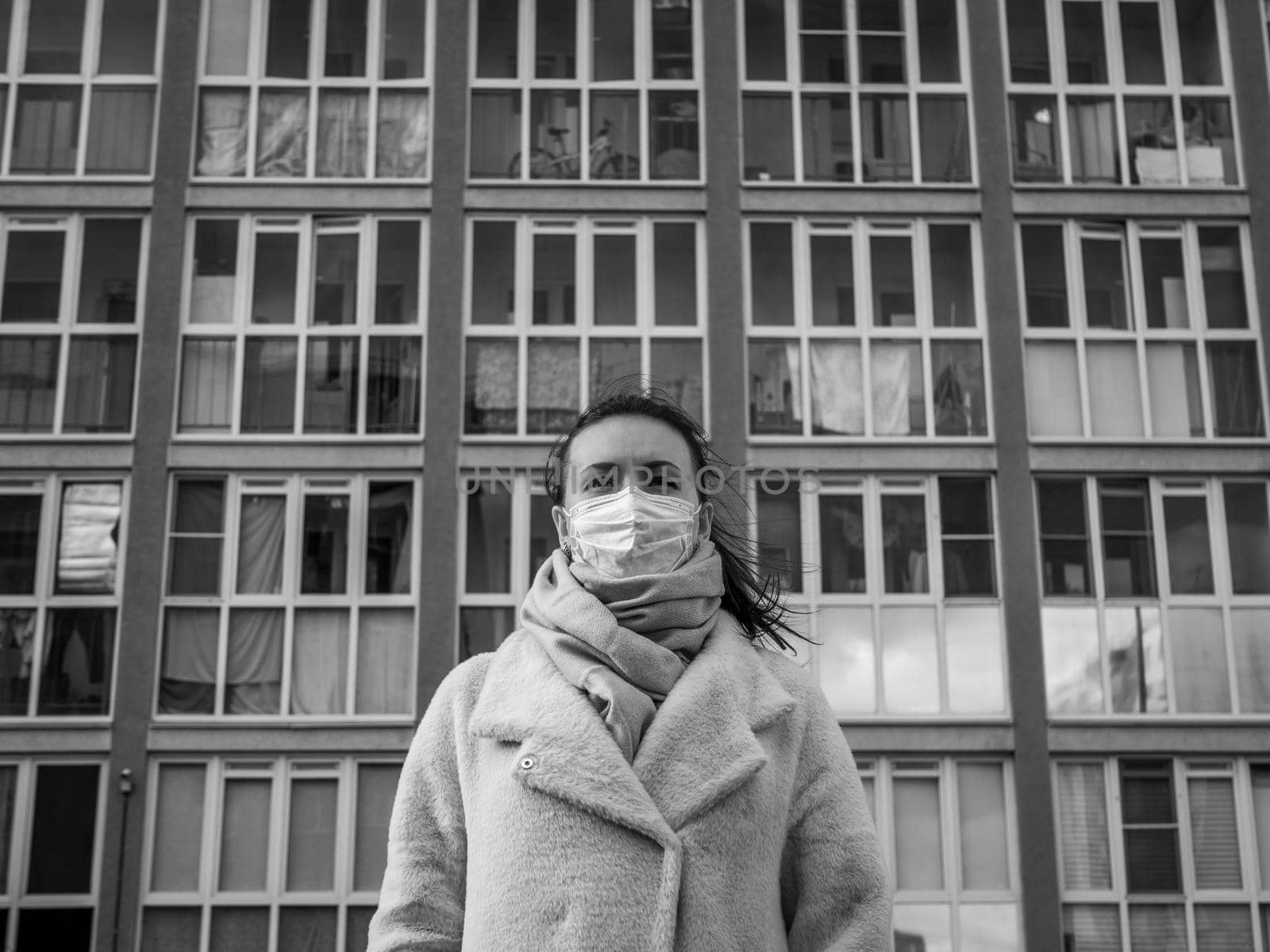 Shot of a girl in wearing face mask for protection, on the street. Against the background of a residential building with windows. lockdown Covid-19 pandemic.