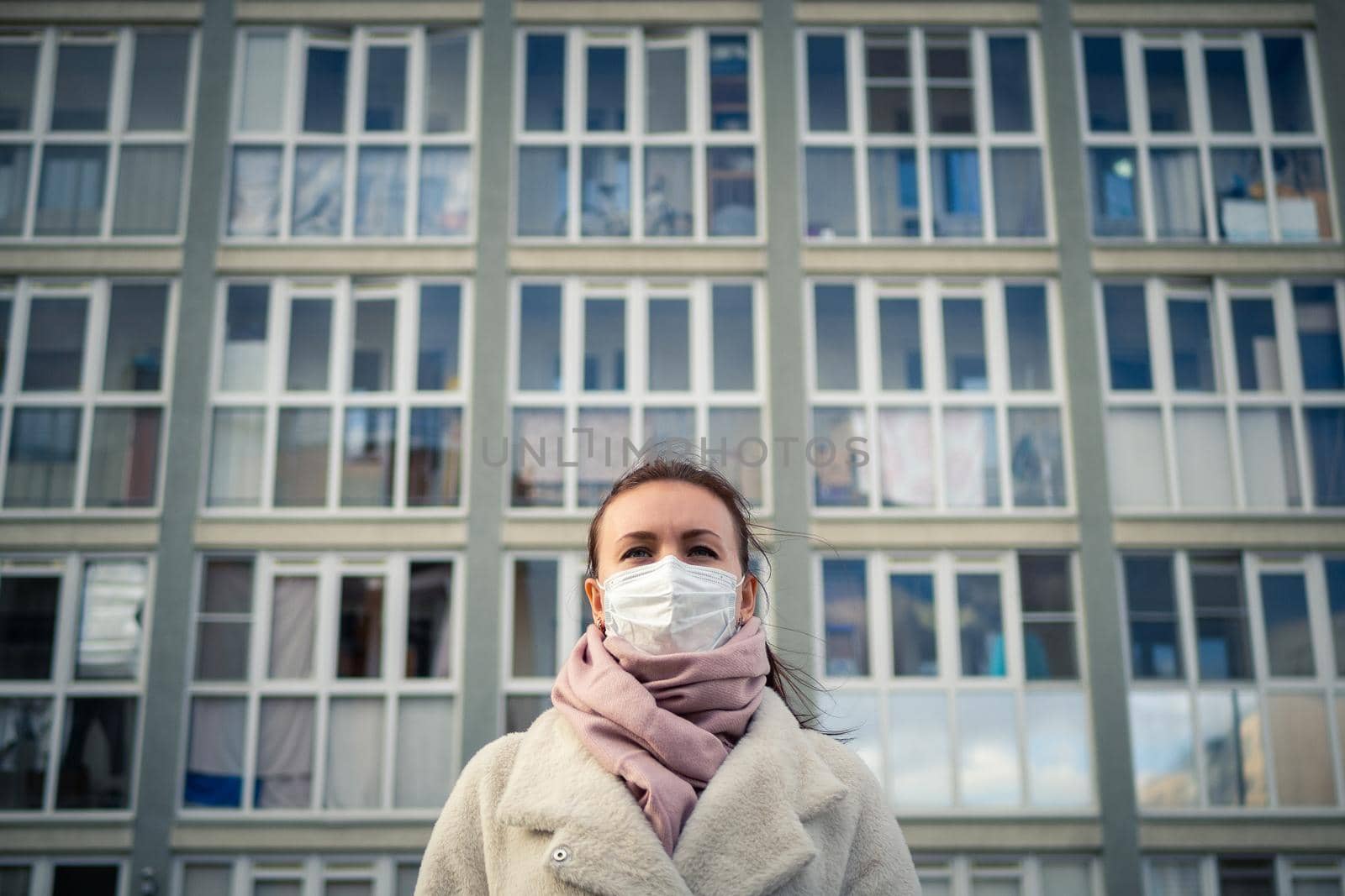 Shot of a girl in wearing face mask for protection, on the street. Against the background of a residential building with windows. lockdown Covid-19 pandemic.