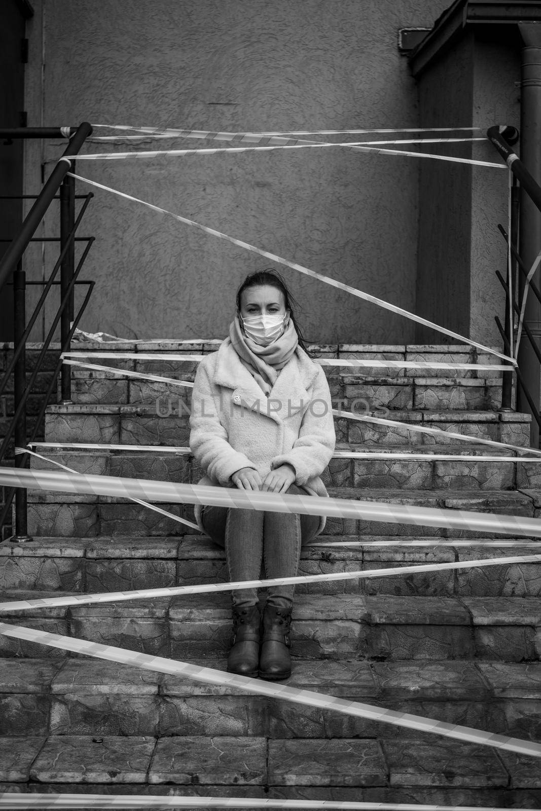 Photo of a girl in a mask. Sitting on the street with danger warning tapes. isolated Covid-19 pandemic.