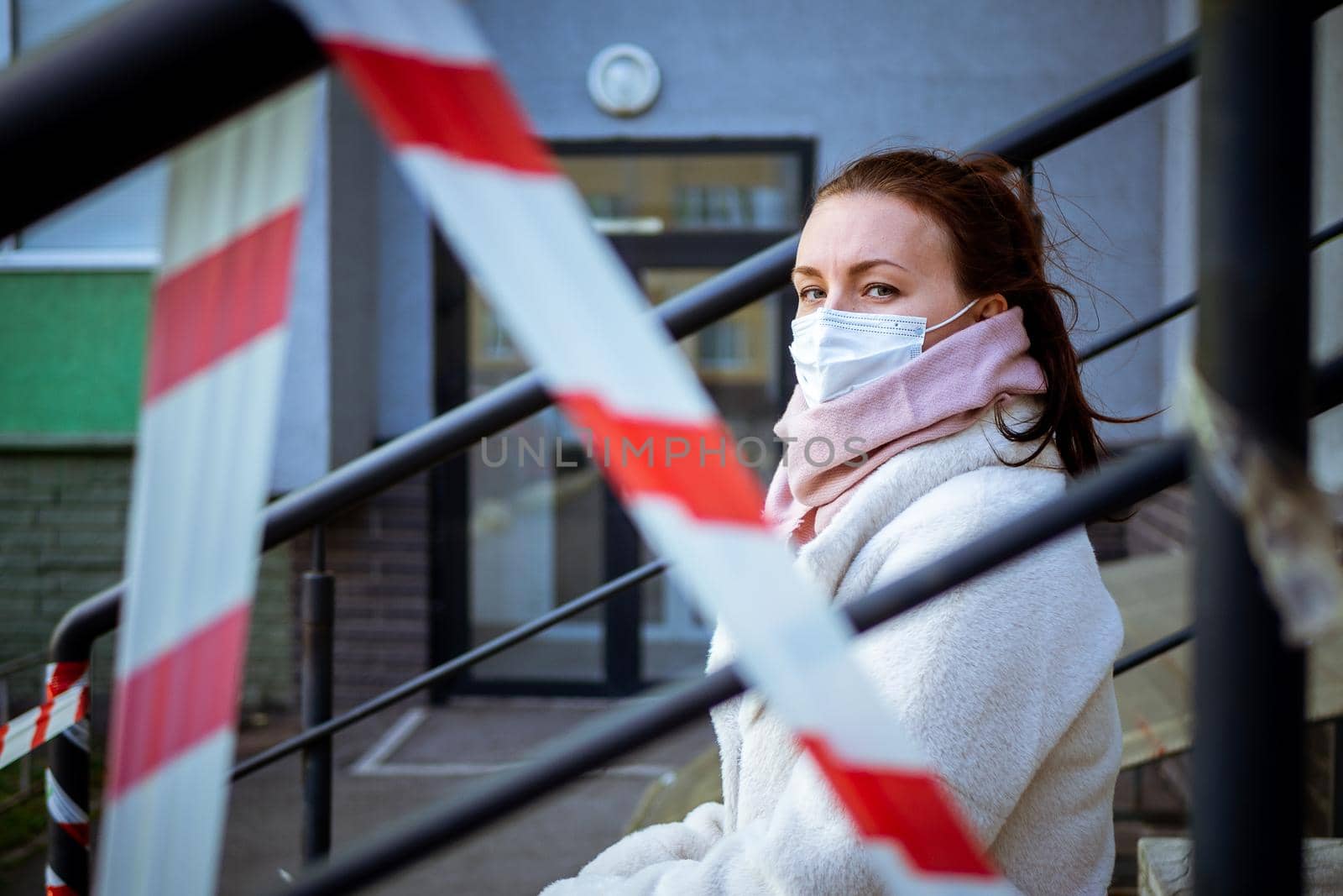 Photo of a girl in a mask. Sitting on the street with danger warning tapes. isolated Covid-19 pandemic.