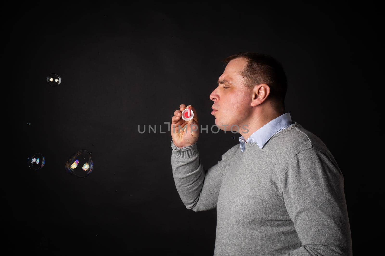 handsome man in a suit is blowing soap bubbles. isolated on a black background