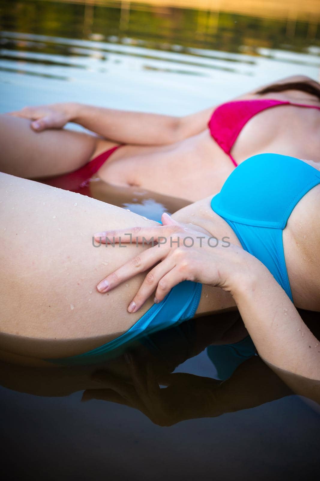 Rear view of two young women with beautiful bodies in bikinis. Blue and pink swimsuit in the water.